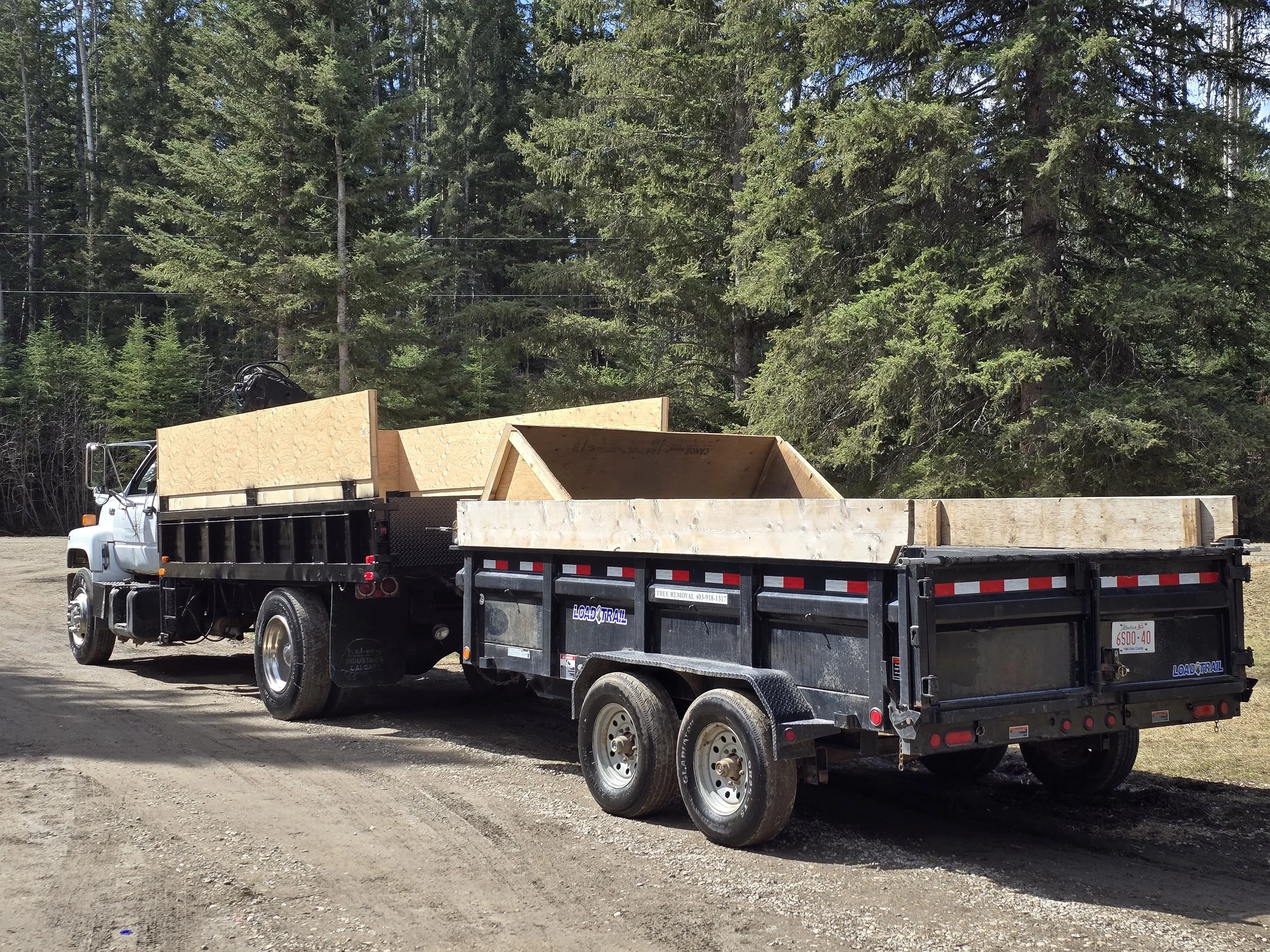 A truck with a flatbed trailer loaded with wooden frames, parked on a dirt road near a forest.