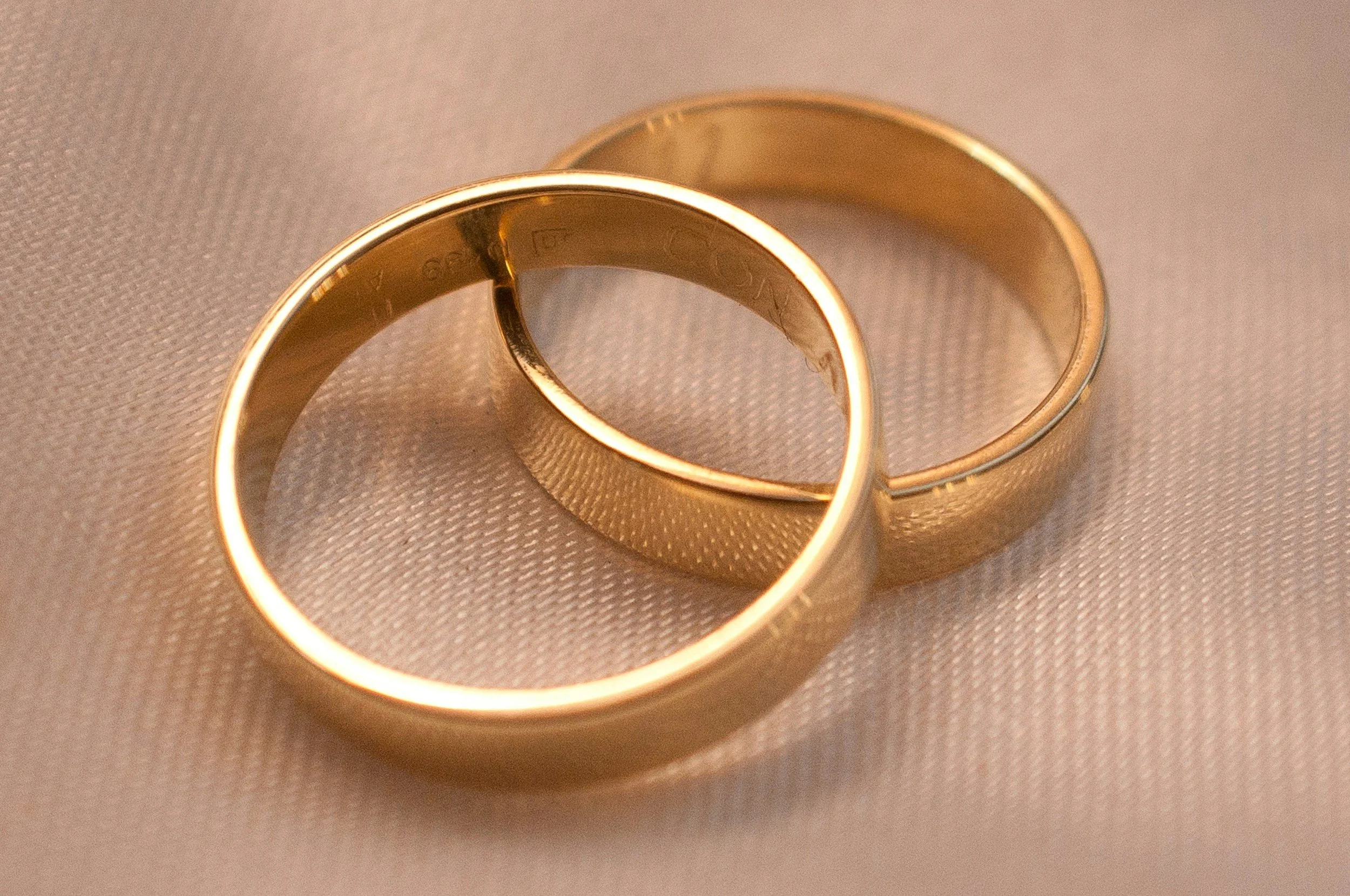 Close-up of two gold wedding bands on a textured pink surface.