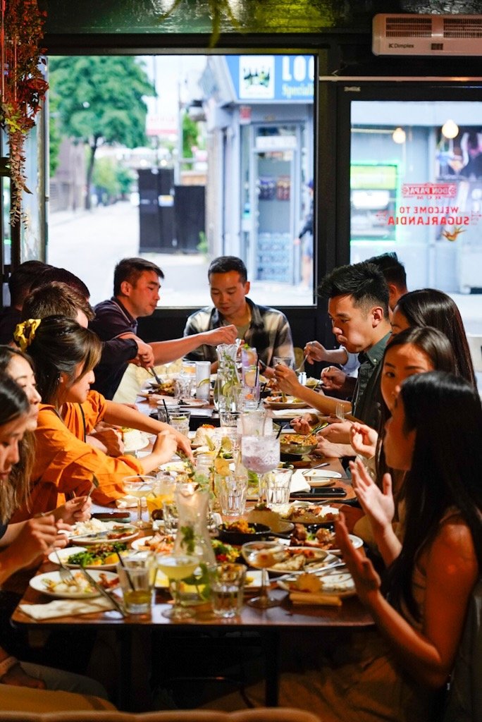 Group of people dining together at a restaurant table, enjoying a variety of dishes in a lively atmosphere.