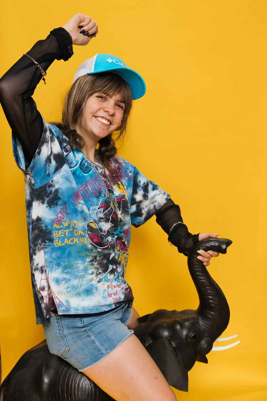 Smiling girl with long hair posing playfully against a light gray wall, wearing a floral-patterned shirt.