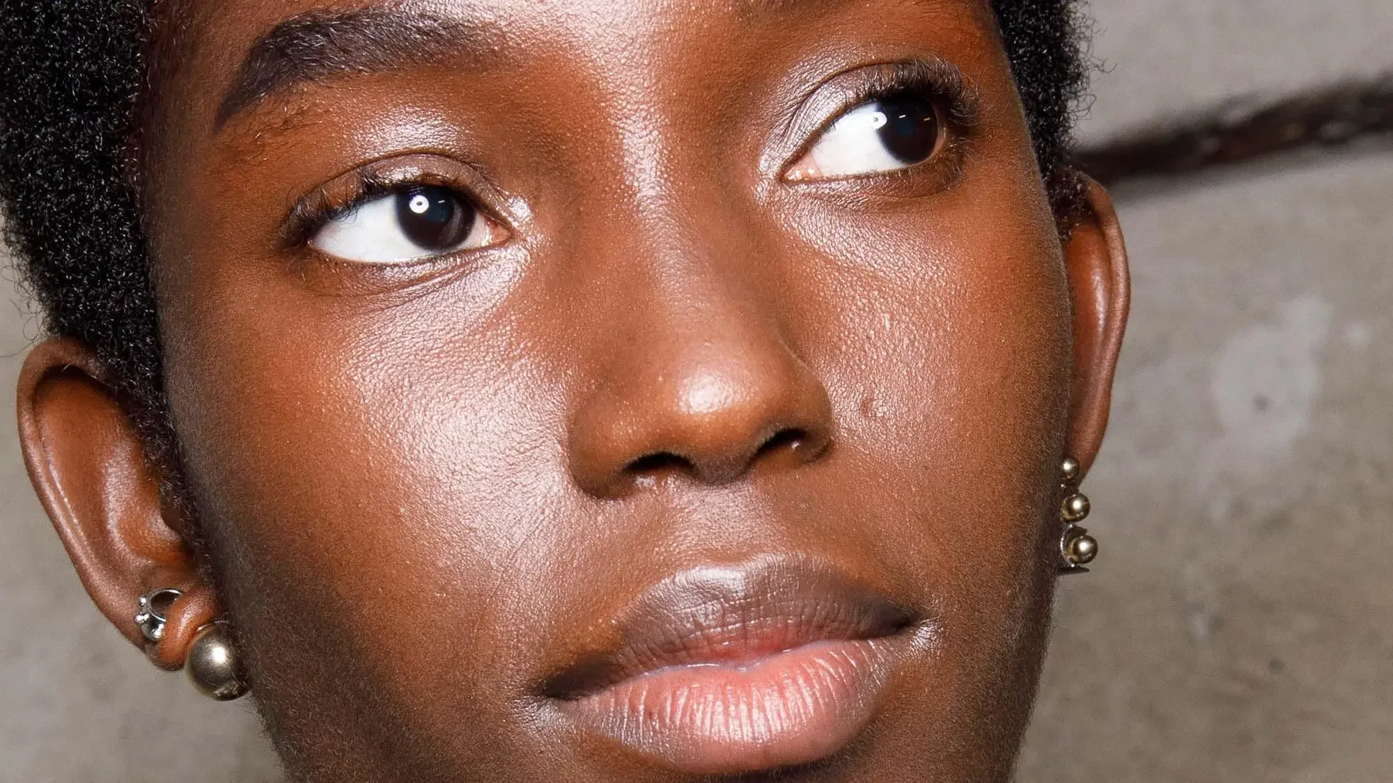 Close-up of a young Black woman with natural hair, wearing earrings, looking slightly upwards.