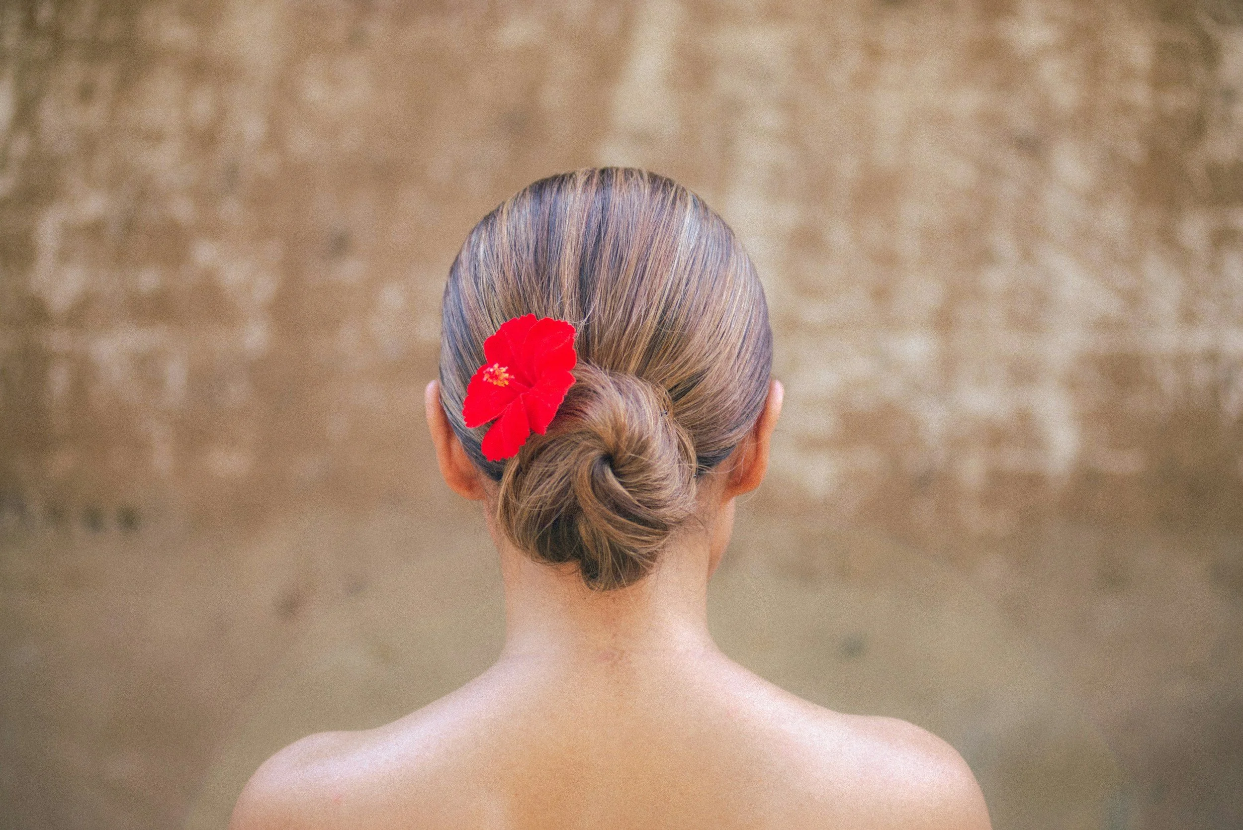 Elegant low bridal updo with a red flower hair accessory, showcasing a classic hairstyle for weddings and special events at Inwood Hair Studio in Manhattan, New York.