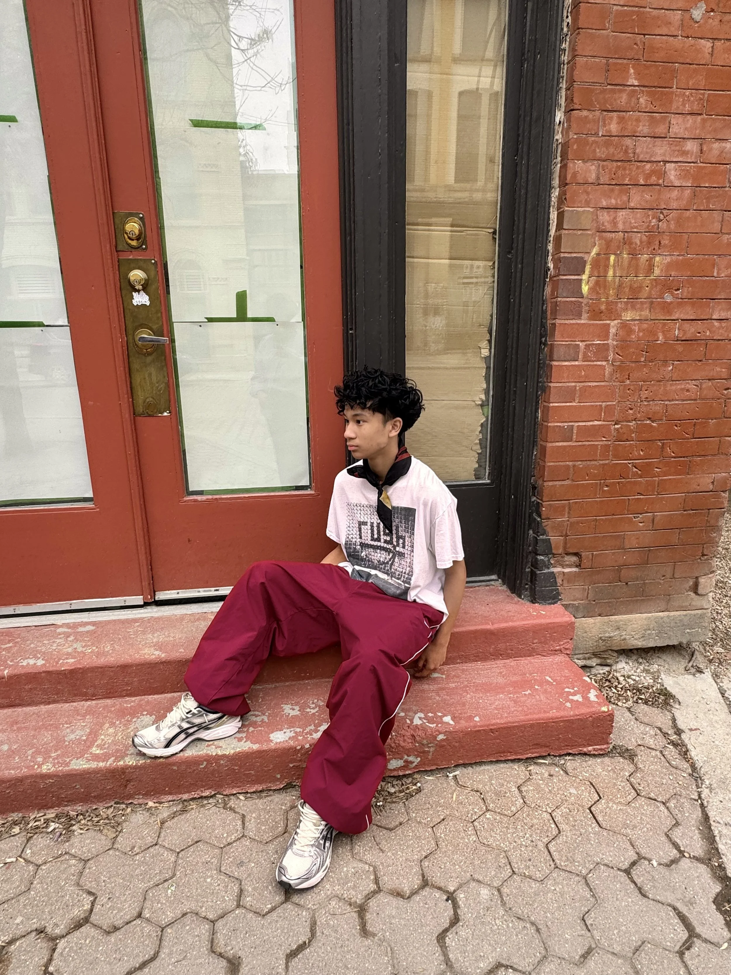 Person in casual clothing sitting on red steps in front of a brick building with red doors and large windows.