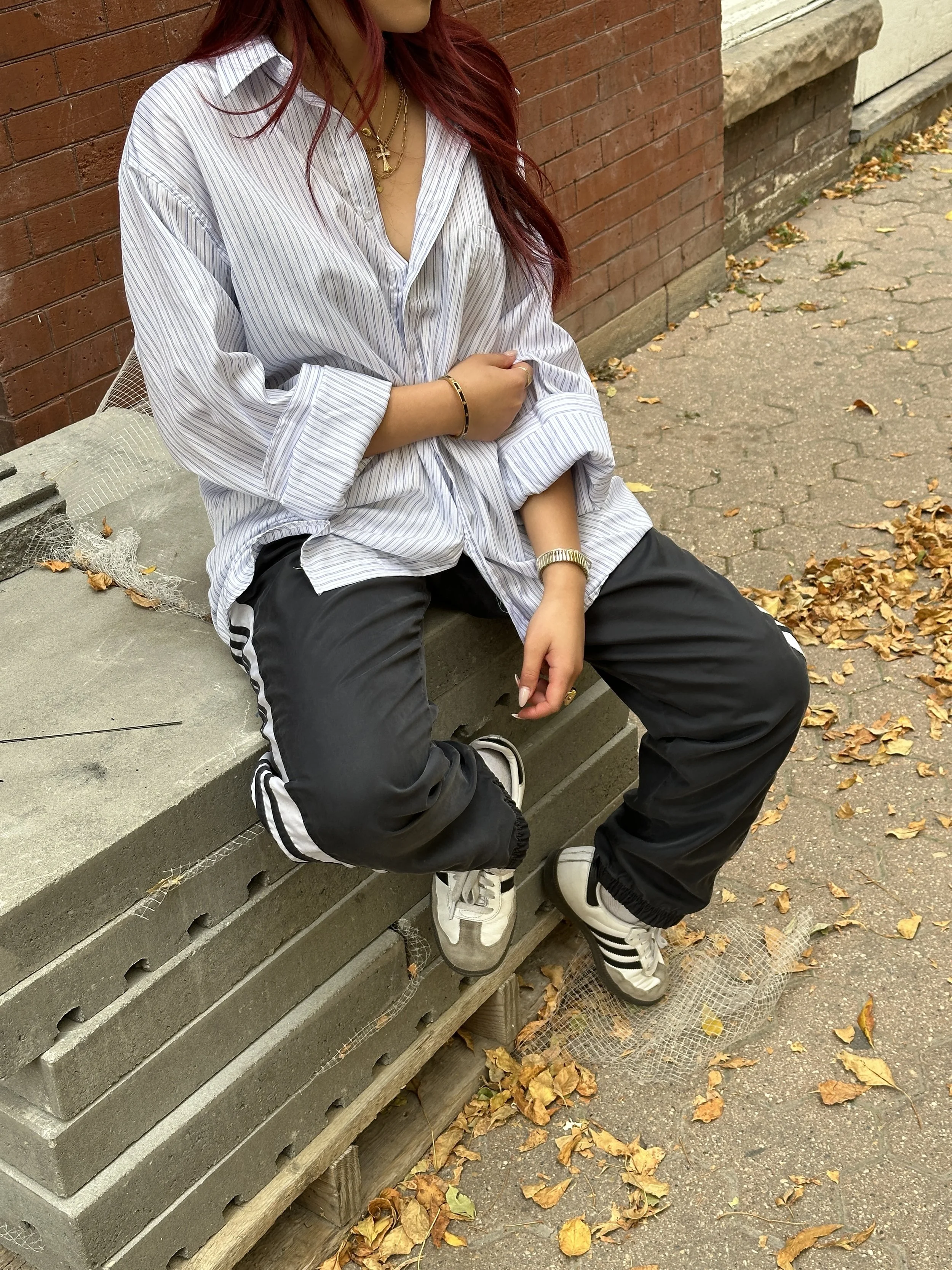 Person sitting on stacked concrete blocks, wearing a striped shirt, black pants, and sneakers, surrounded by fallen leaves.