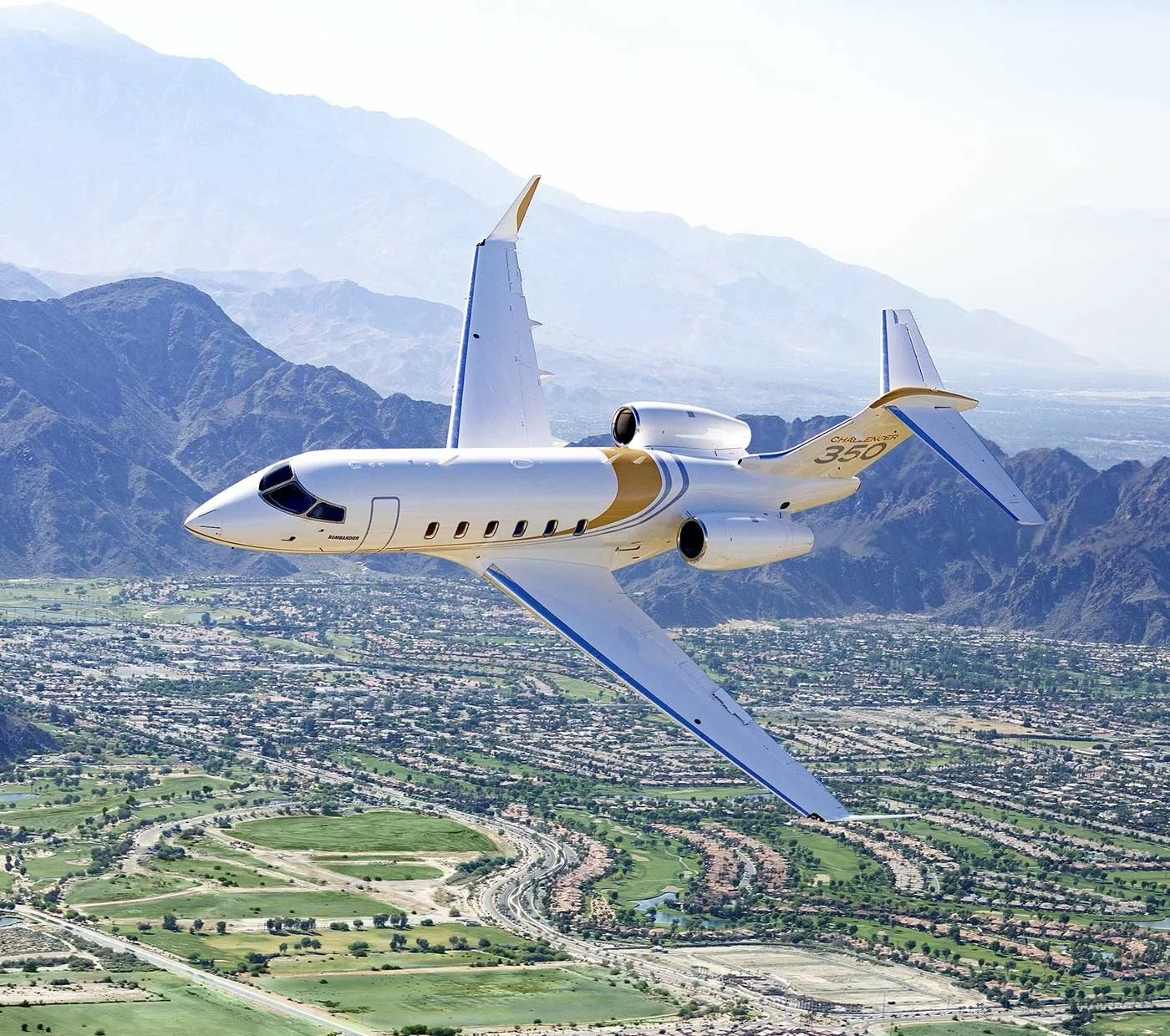 Private jet flying over a landscape with mountains and a city below.