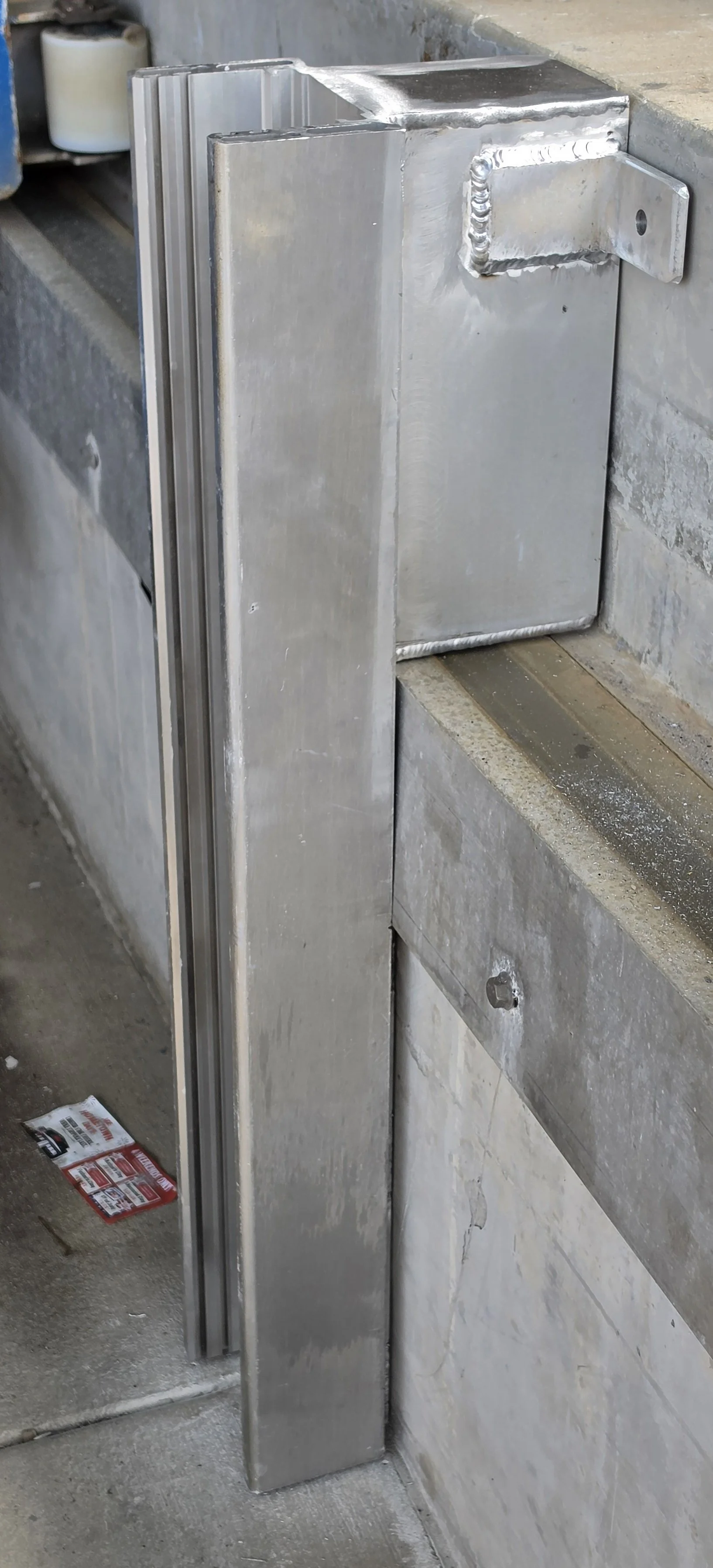 Custom fabricated flood barrier bracket for a drive pit of a dry boat storage barn