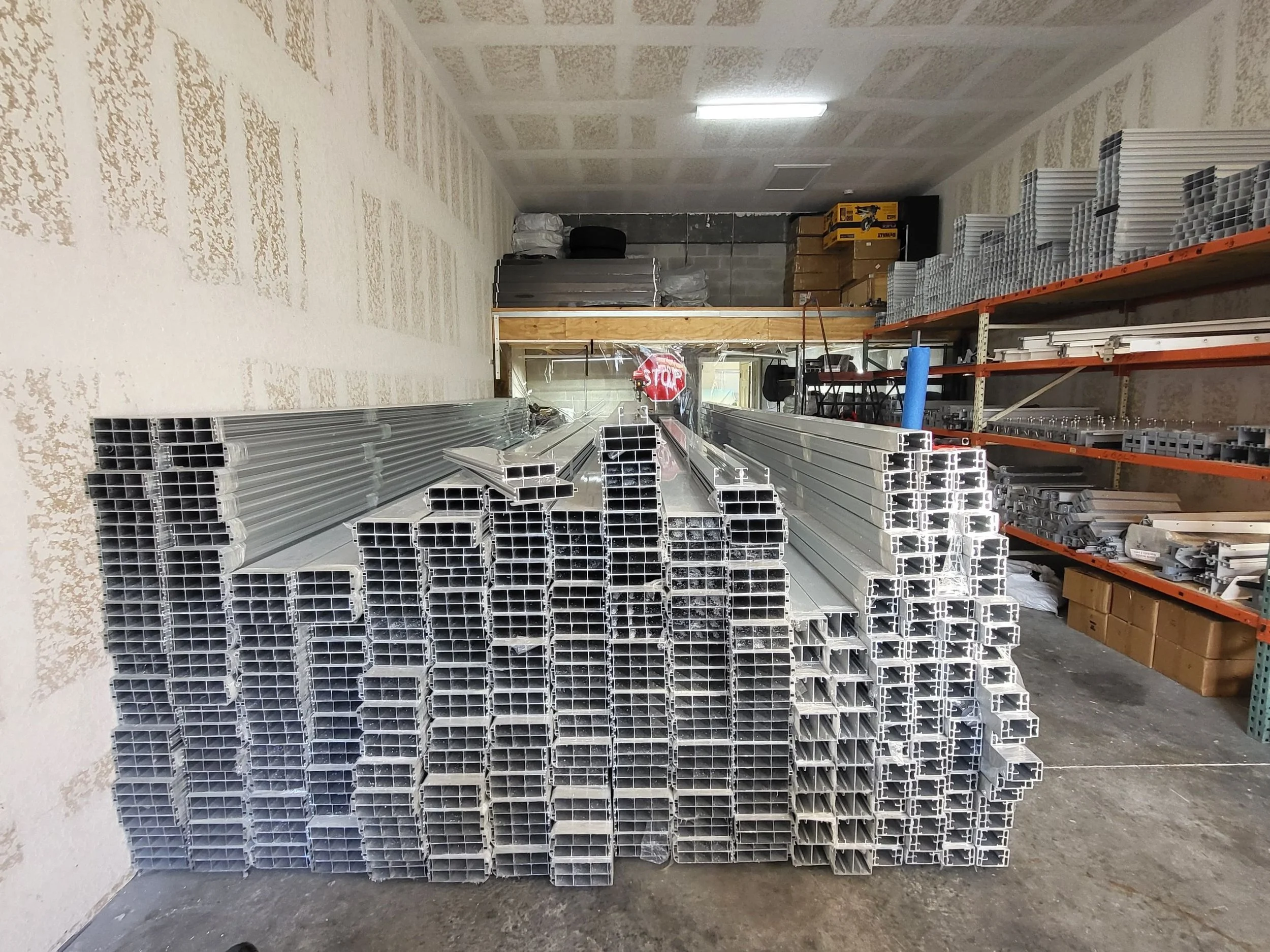 Metal pipes and tubing stacked on orange shelving in a storage room.