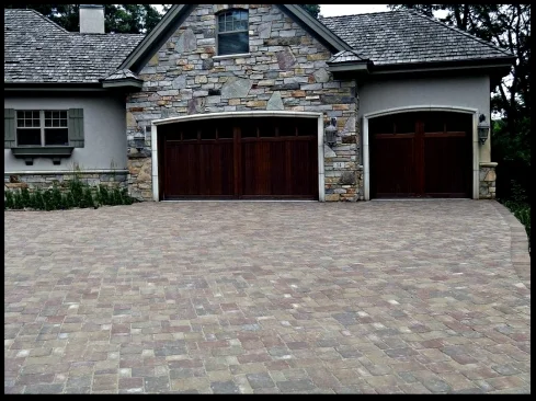 House with stone facade, two wooden garage doors, and a patterned brick driveway.