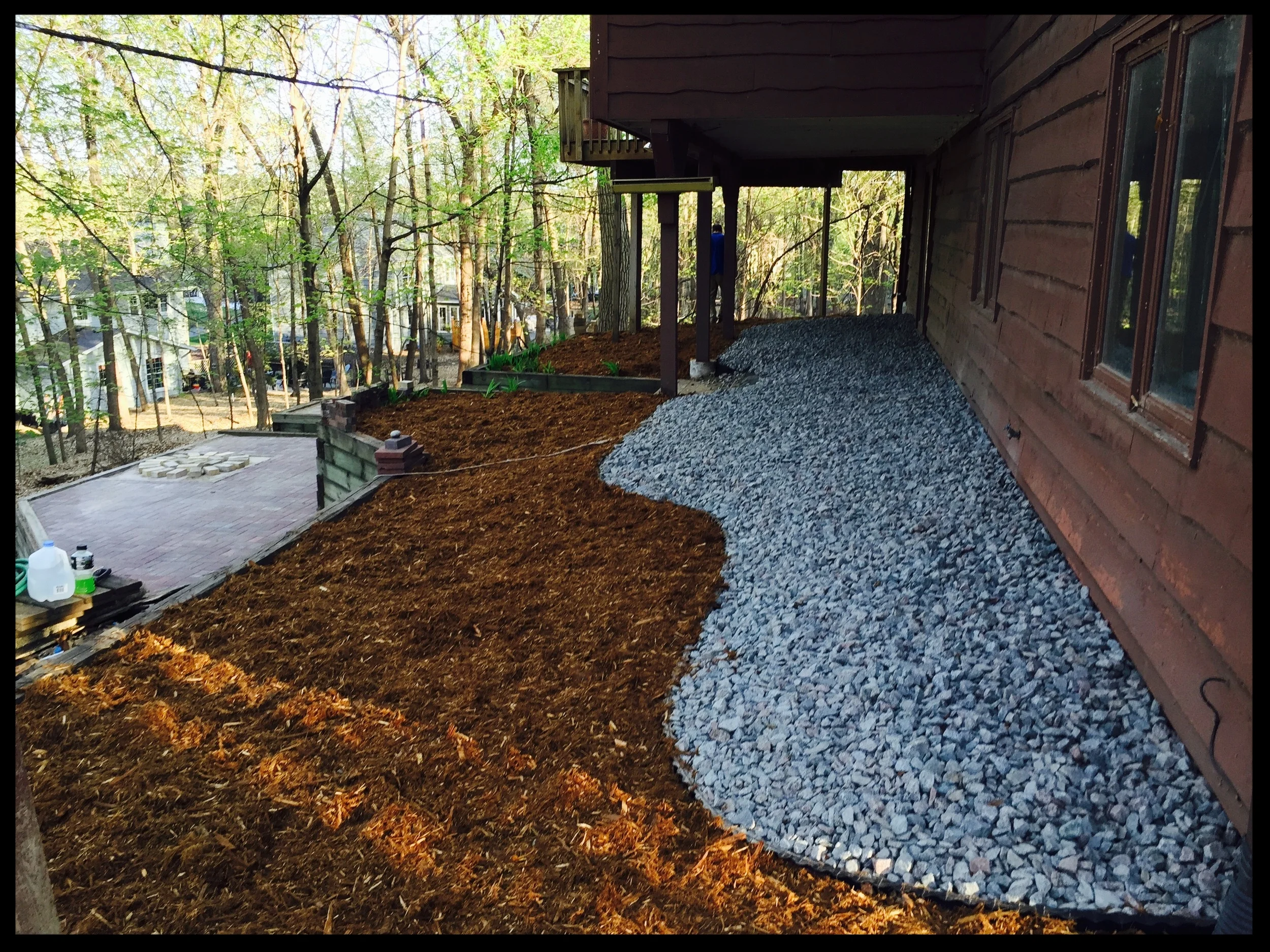 Backyard under construction with a mulched garden bed, gravel pathway, and trees in the background.