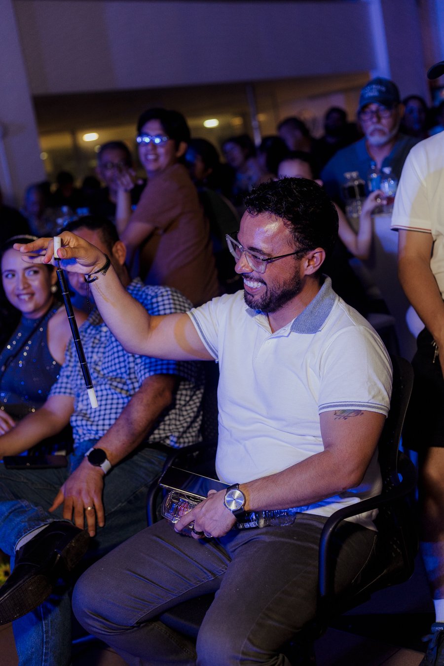 Hombre sosteniendo un objeto pequeño en un evento con público presente.