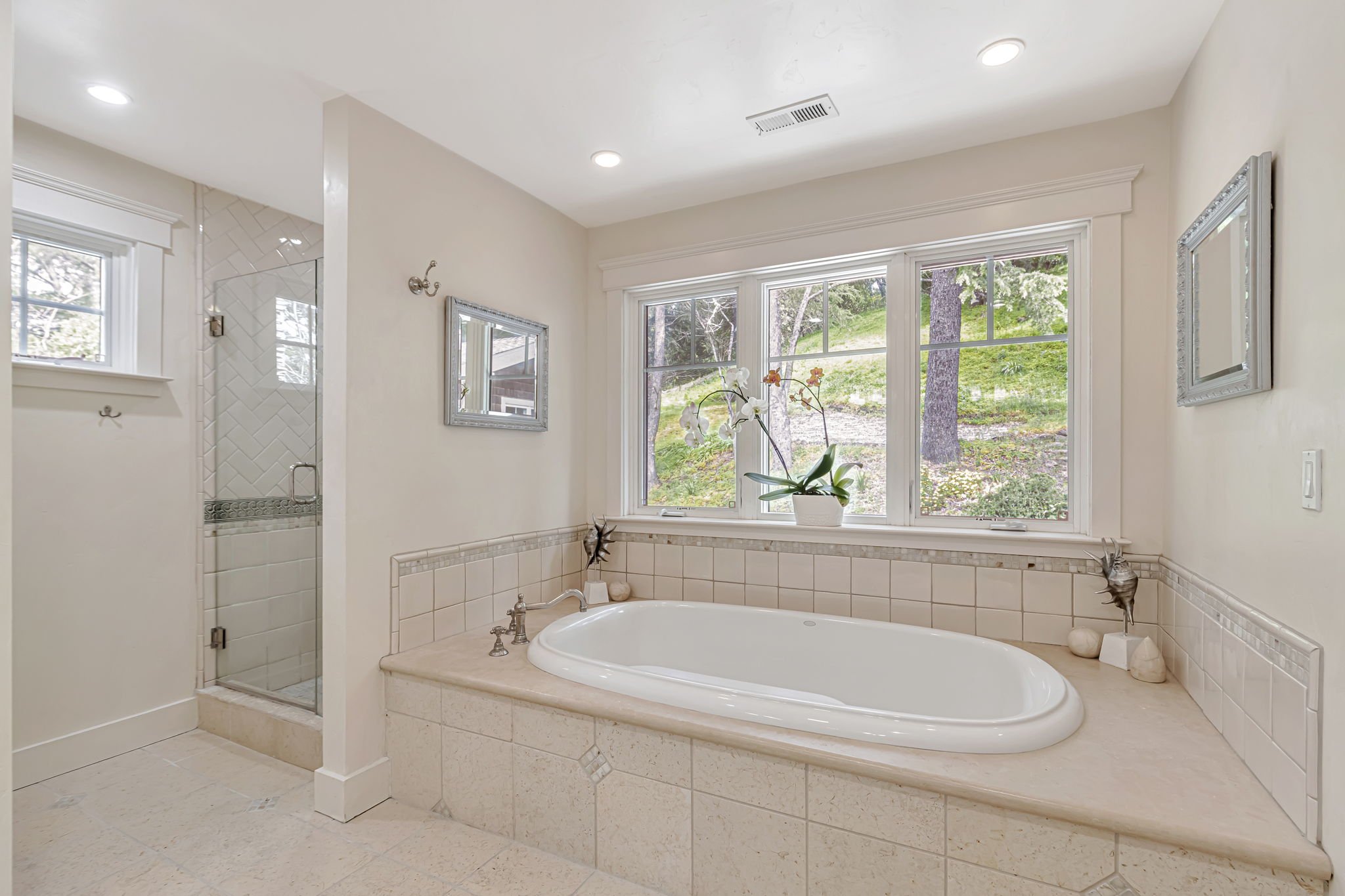 Bathroom with large window, freestanding bathtub, potted orchid, glass shower, and wall mirrors.