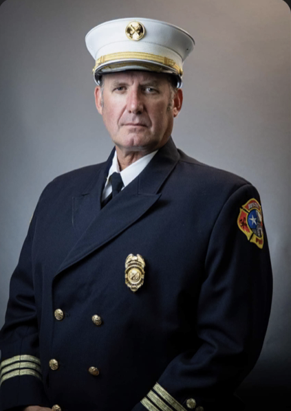 A man in a navy uniform and white cap, with a serious expression, against a plain background.