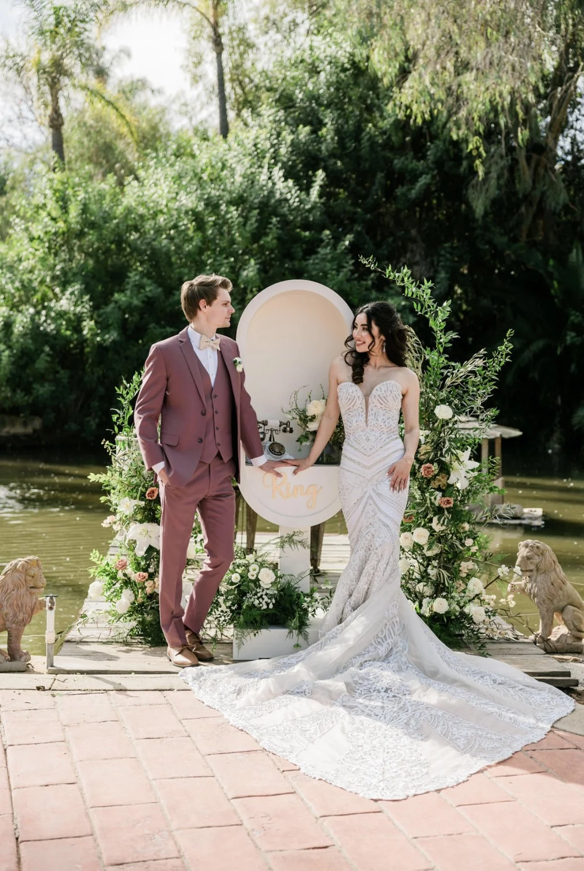 Couple in wedding attire near decorative arch with greenery.