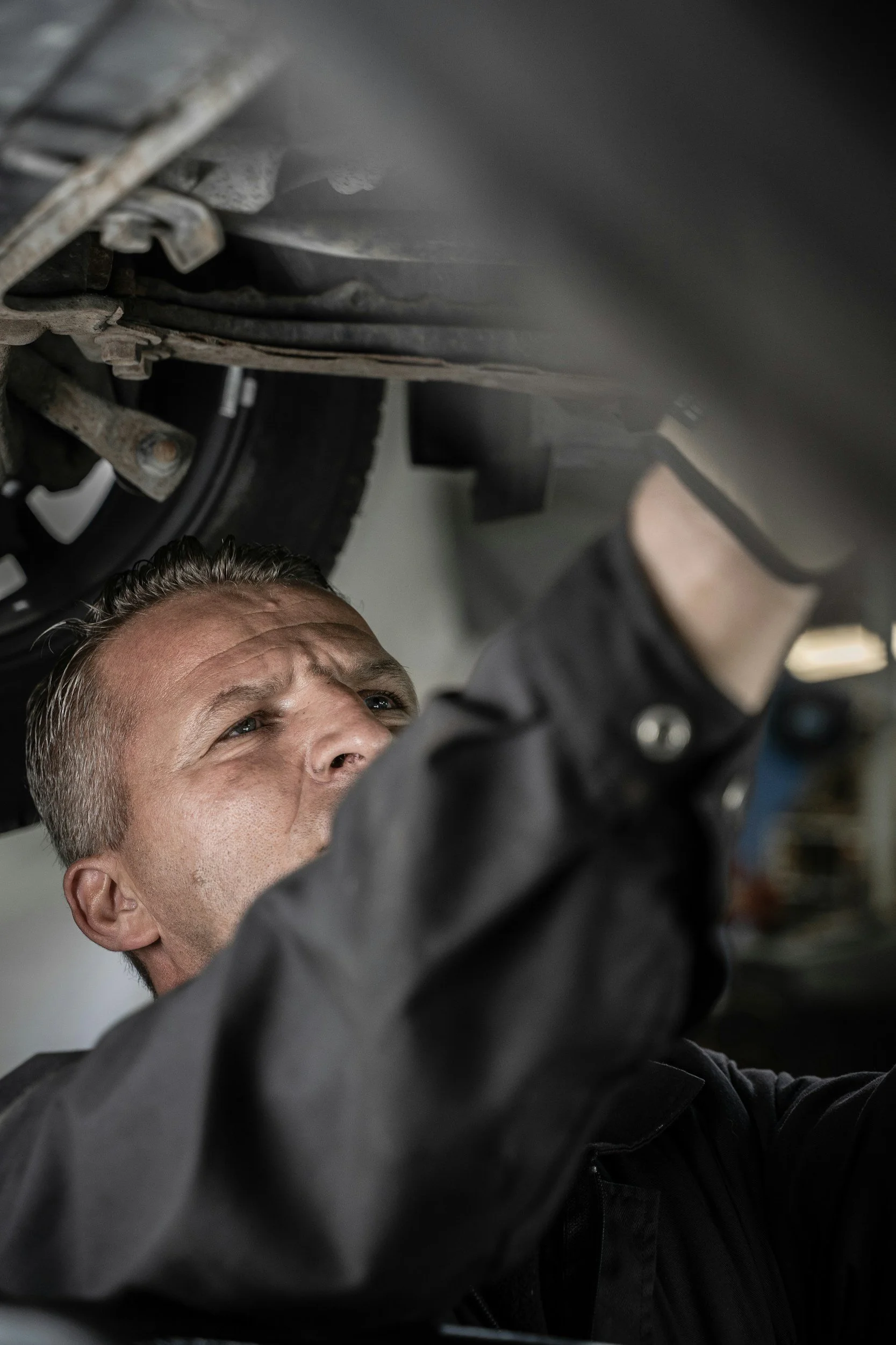 Mechanic working under a vehicle, inspecting or repairing, with a focus on his concentrated expression.