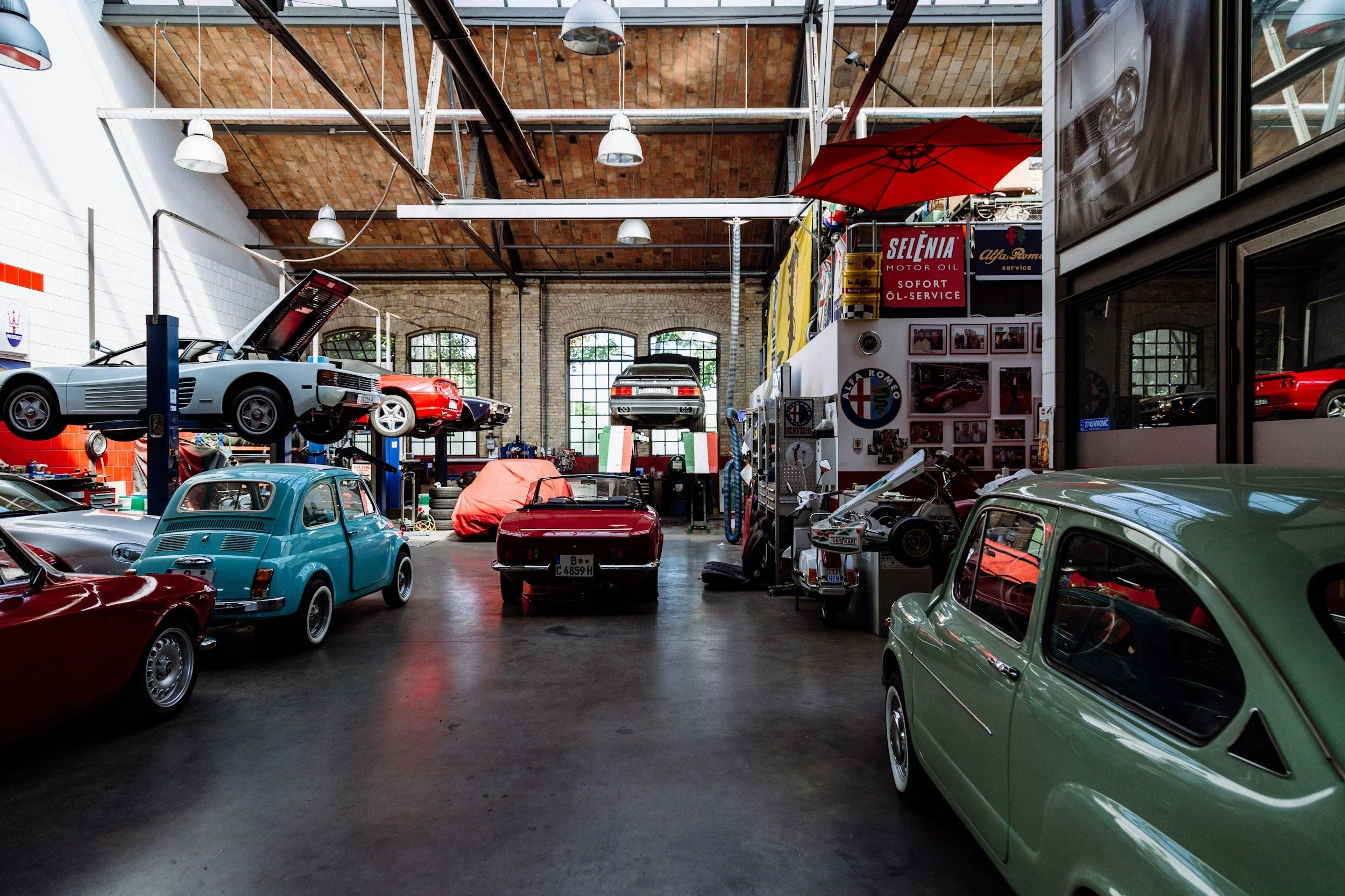 Vintage car workshop interior with classic cars on lifts and various automotive memorabilia on walls.