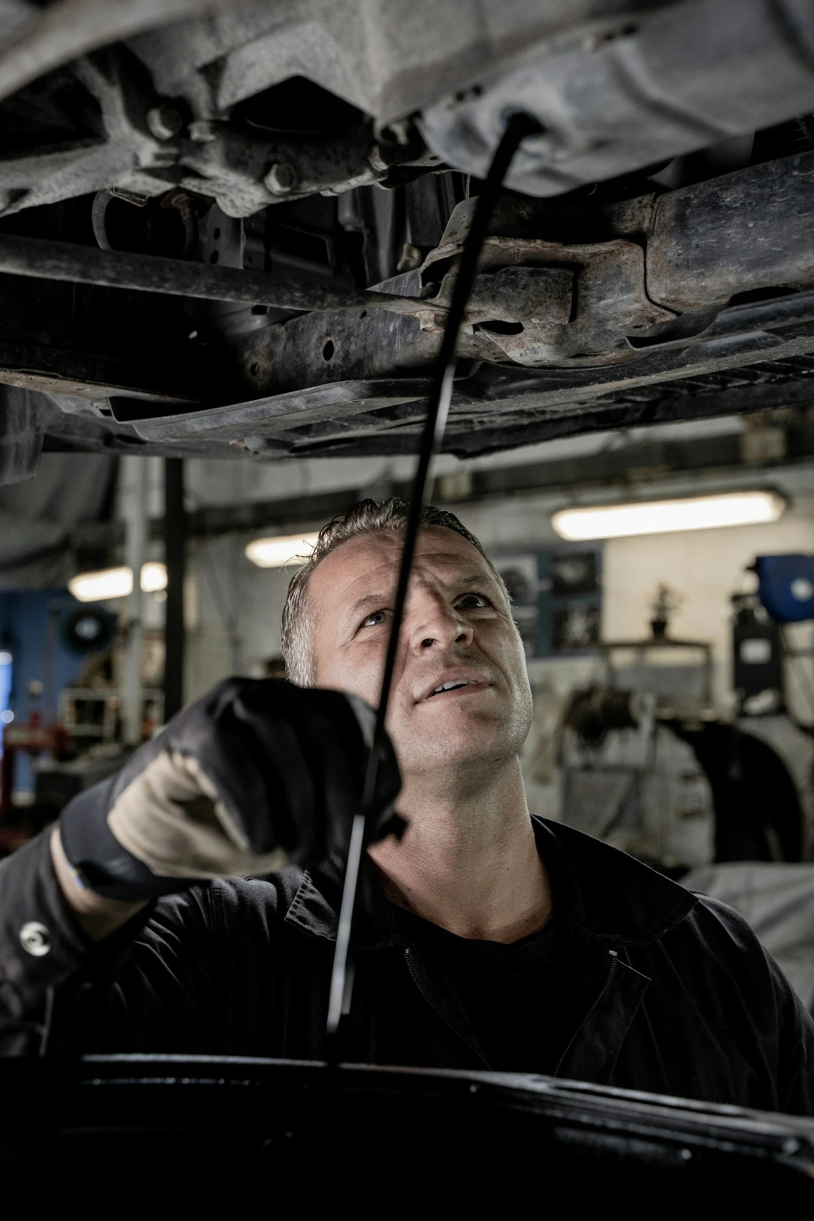 Mechanic checking under a raised vehicle in a garage.