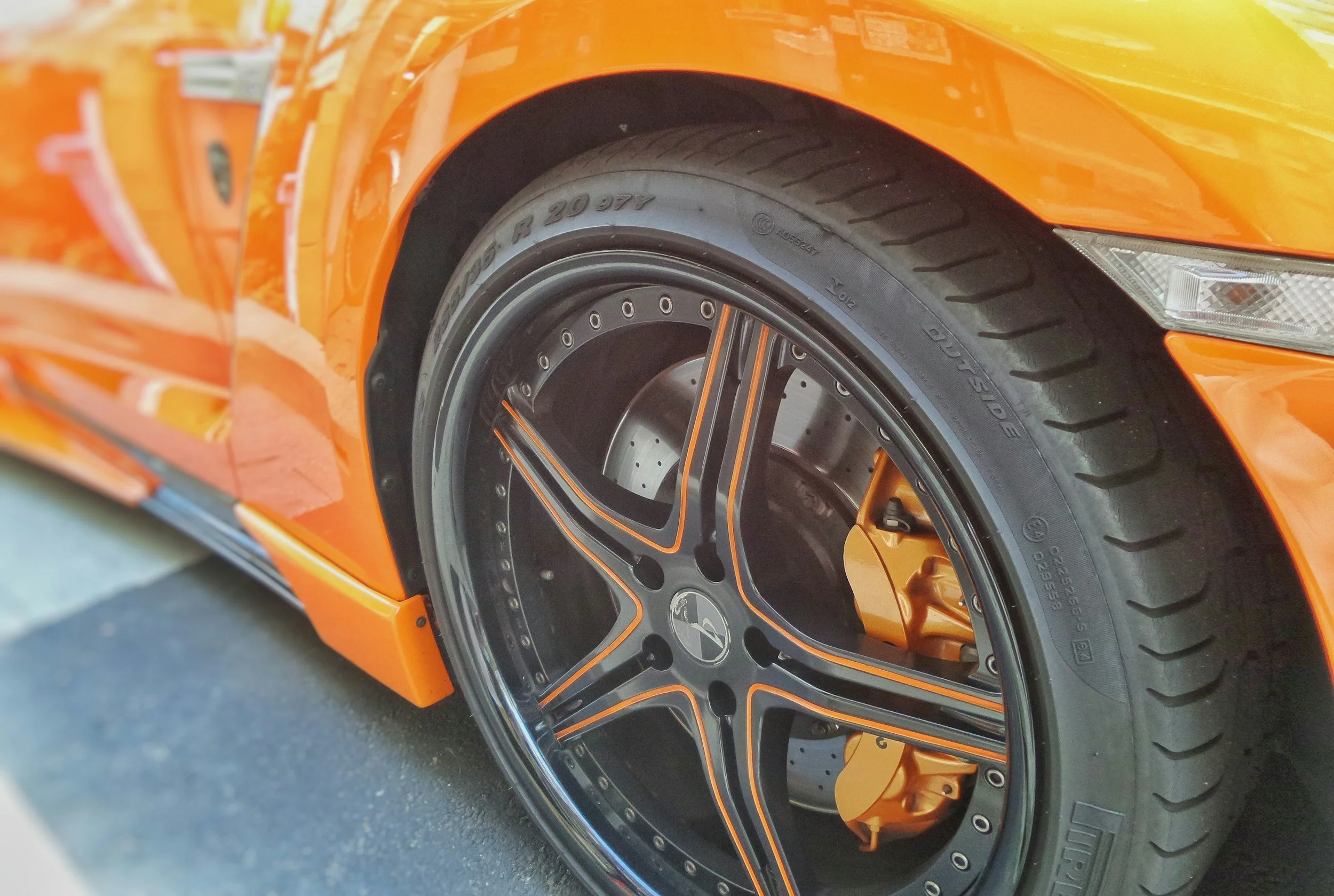 Close-up of an orange sports car wheel with black and orange alloy rims and visible brake caliper.