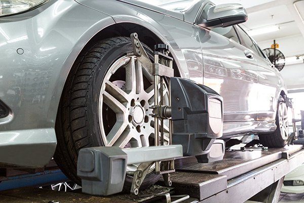 Car undergoing wheel alignment on a hydraulic lift in an auto repair shop.