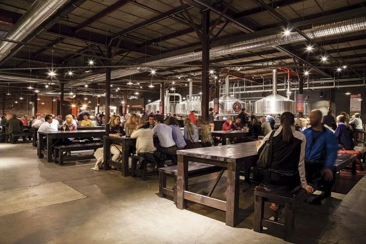 Indoor bierhall with communal tables and brewery tanks.