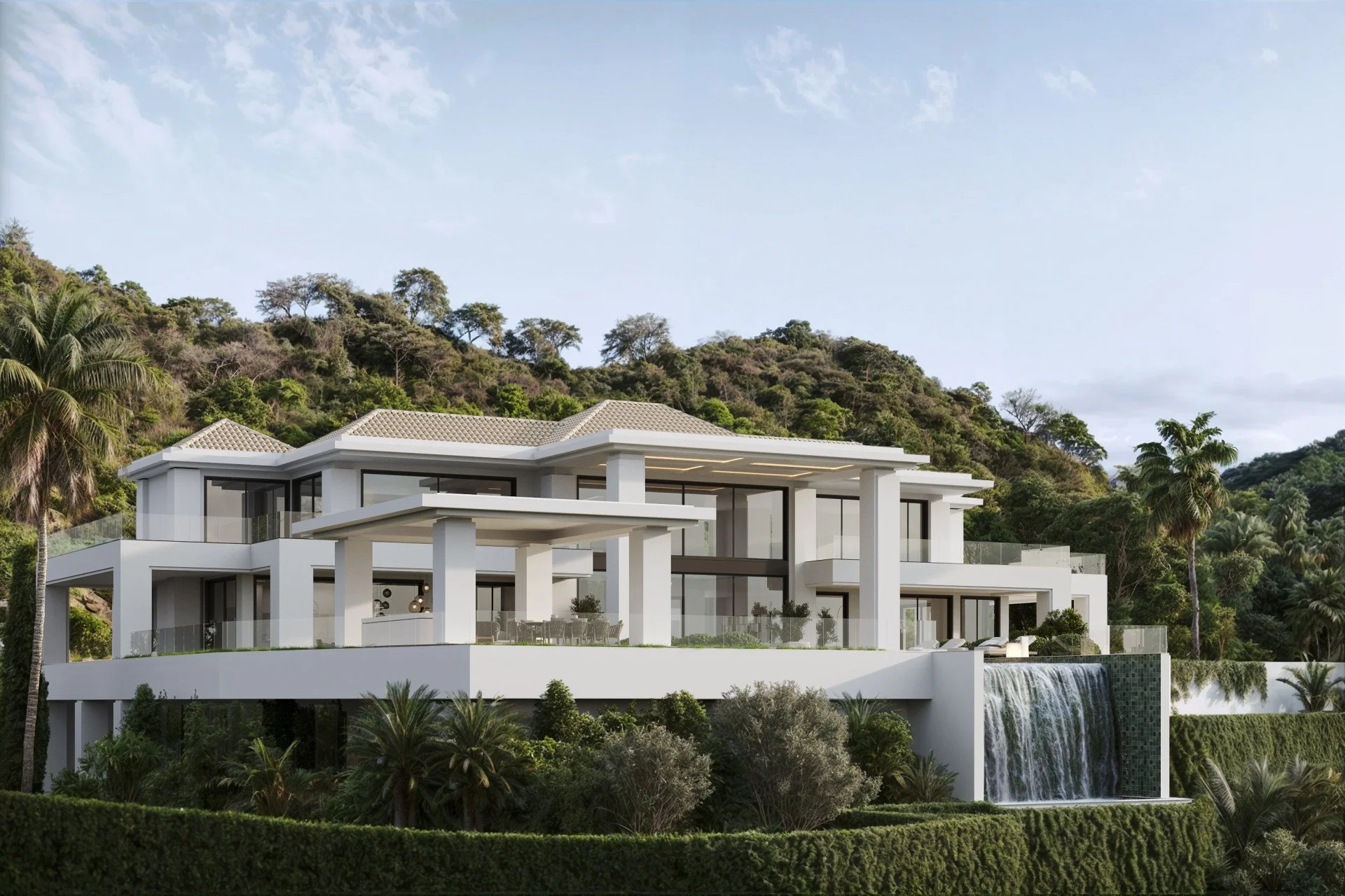 Modern white house with large windows and outdoor living spaces, situated on a hillside with lush greenery and trees, and a waterfall feature in the background.