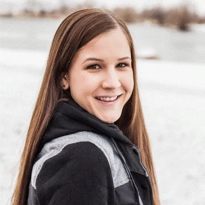 Smiling person wearing a winter jacket outdoors with snowy background.