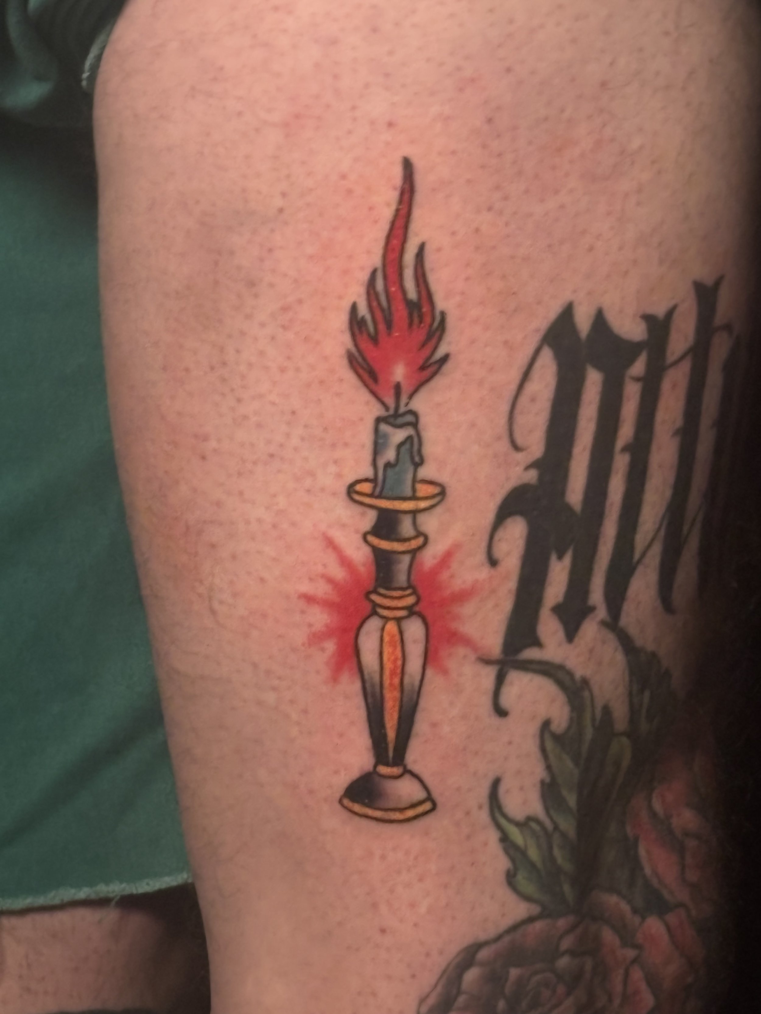 Tattoo of a stylized candle with a red flame, set in a holder.