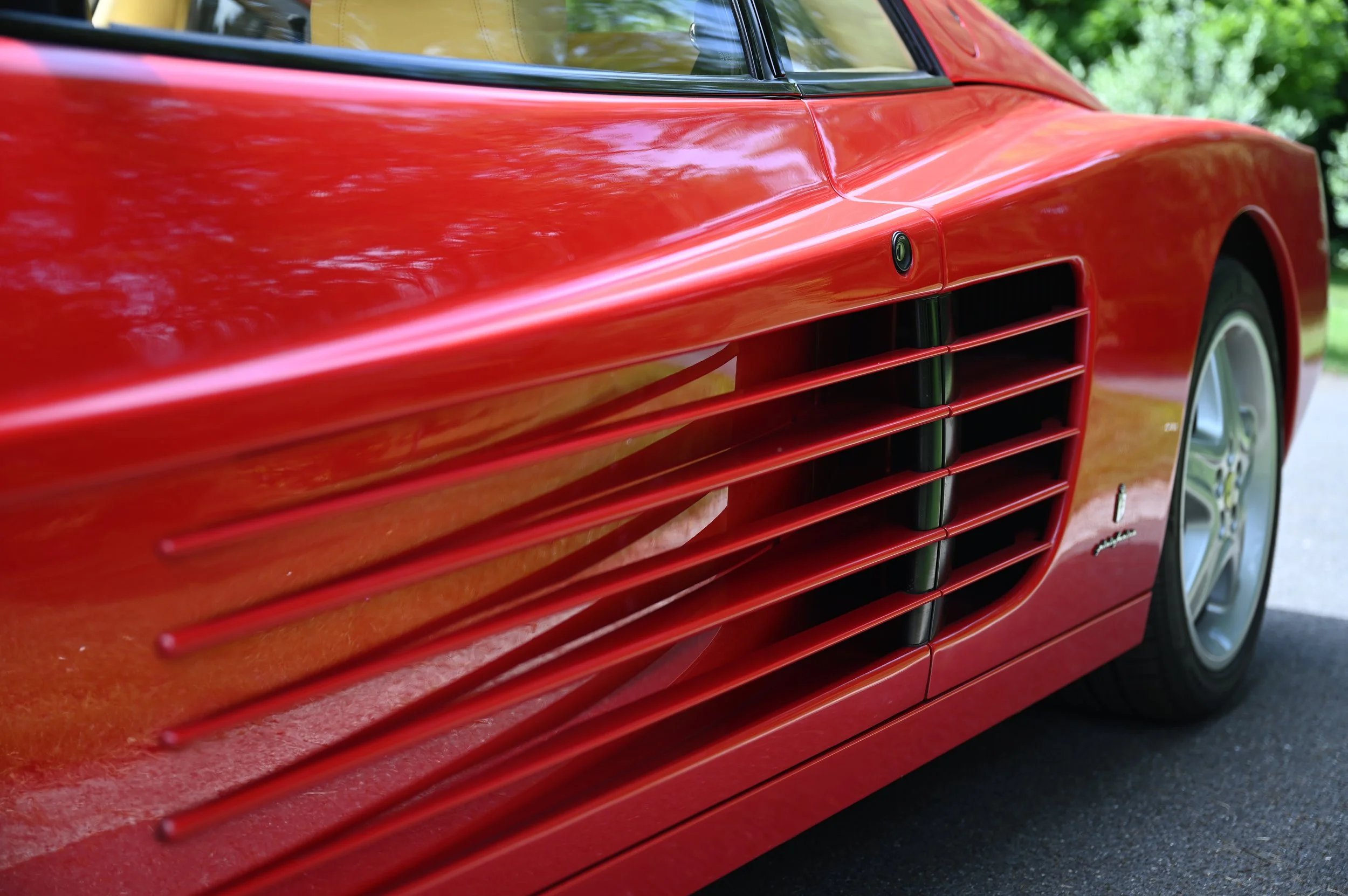 Close-up of a red sports car's side, showing distinctive side vents and a wheel.