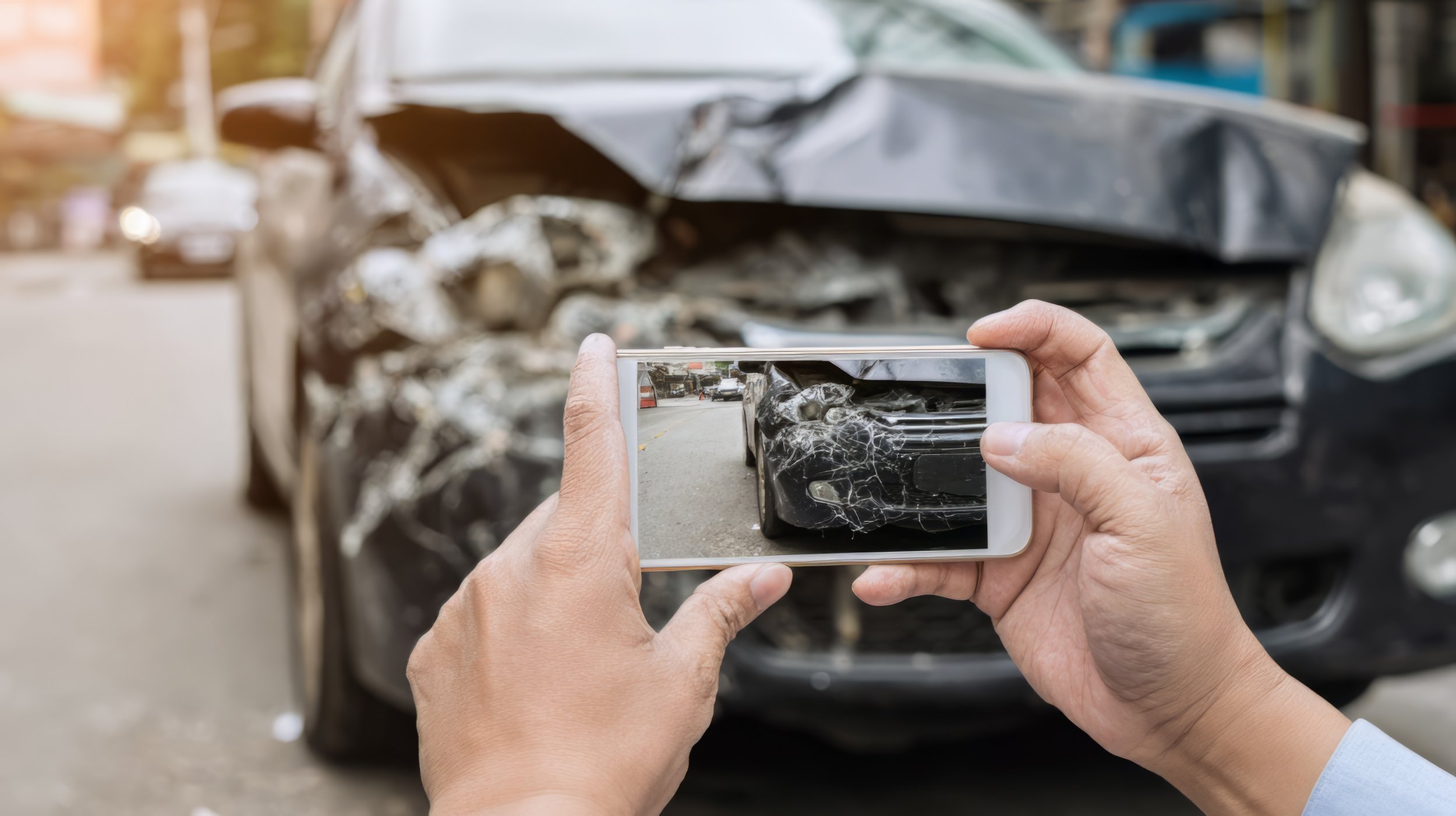 A driver using a smartphone to photograph damage to a vehicle after an accident.
