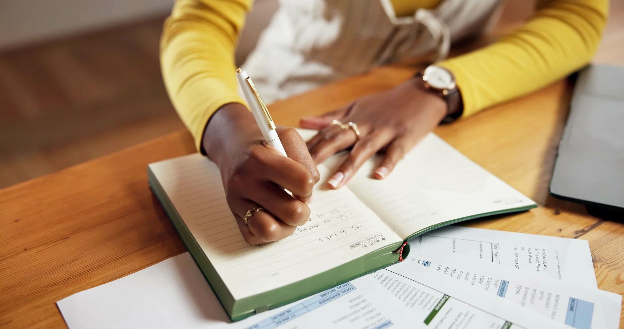 A person writing dated notes in a notebook while reviewing paperwork about a family member's care.