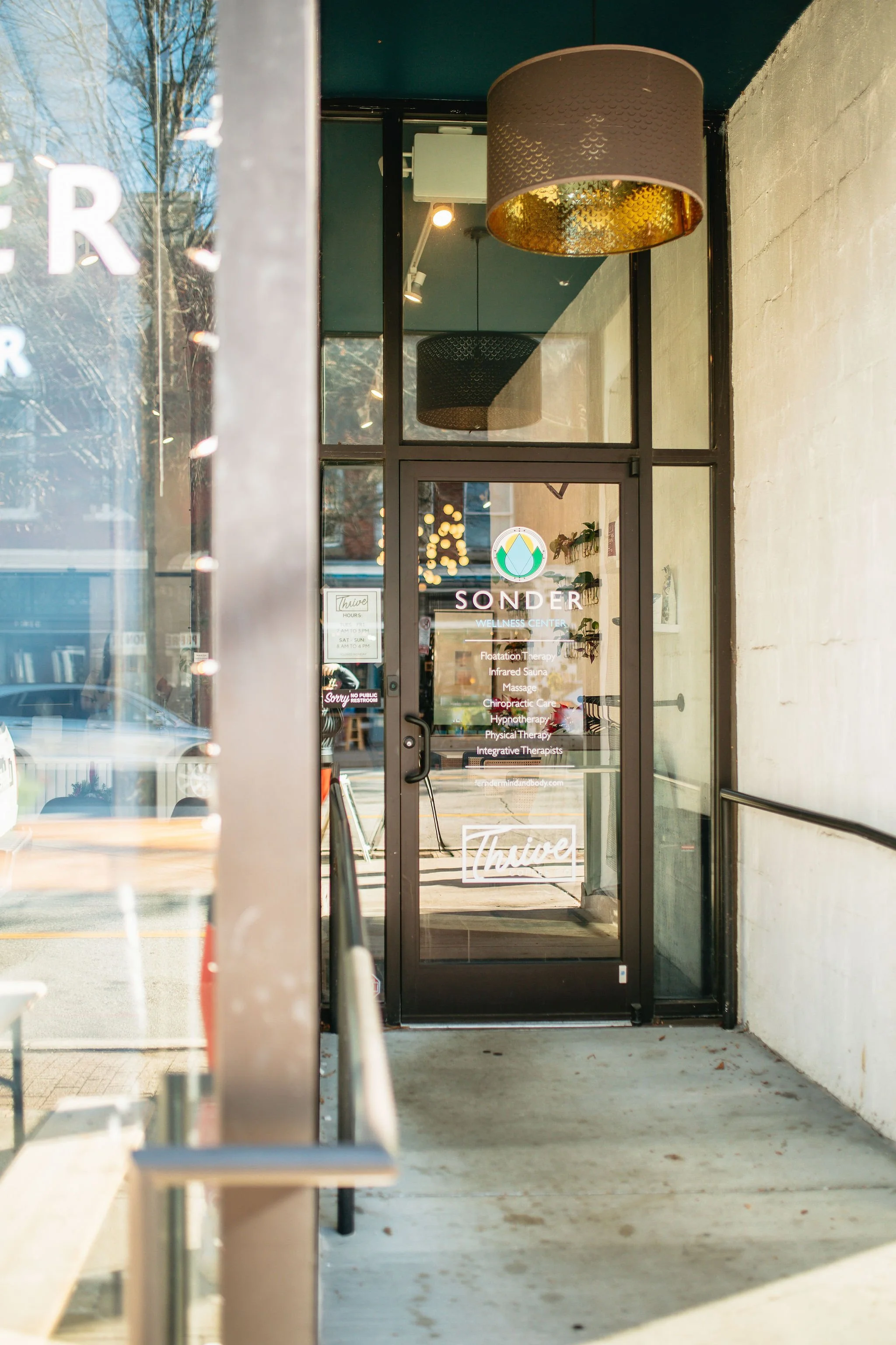Front door of a wellness center named 'Sonder', with services listed on the glass door including floatation therapy, infrared sauna, massage, chiropractic care, hypnotherapy, physical therapy, and integrative therapists.