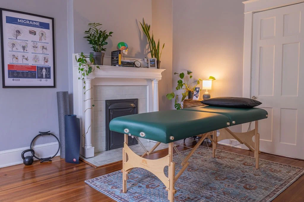 Migraine specialist office with massage table and migraine diagram on wall, with antique fireplace in background