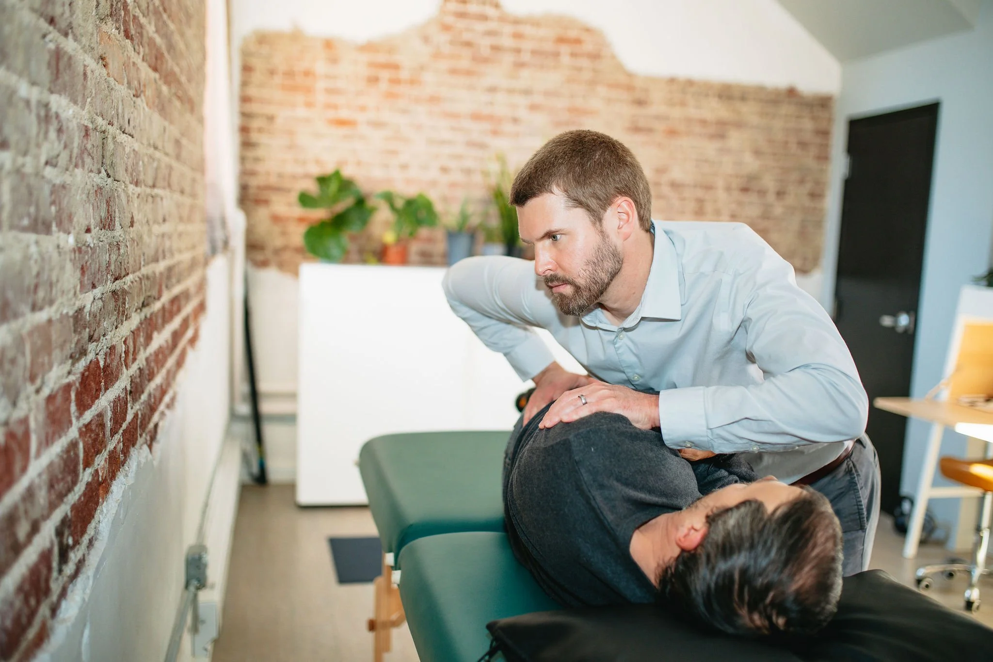 Chiropractor adjusting a patient's neck during a session in a professional clinic with brick walls and plants in the background.