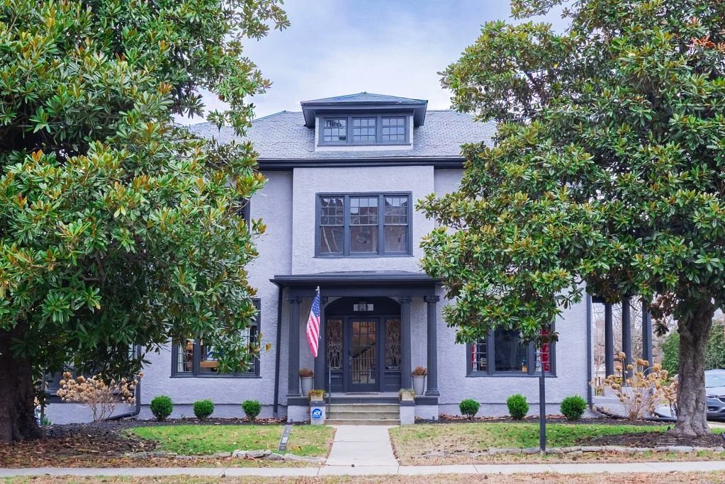 Grey 1920s building with two magnolia trees in front