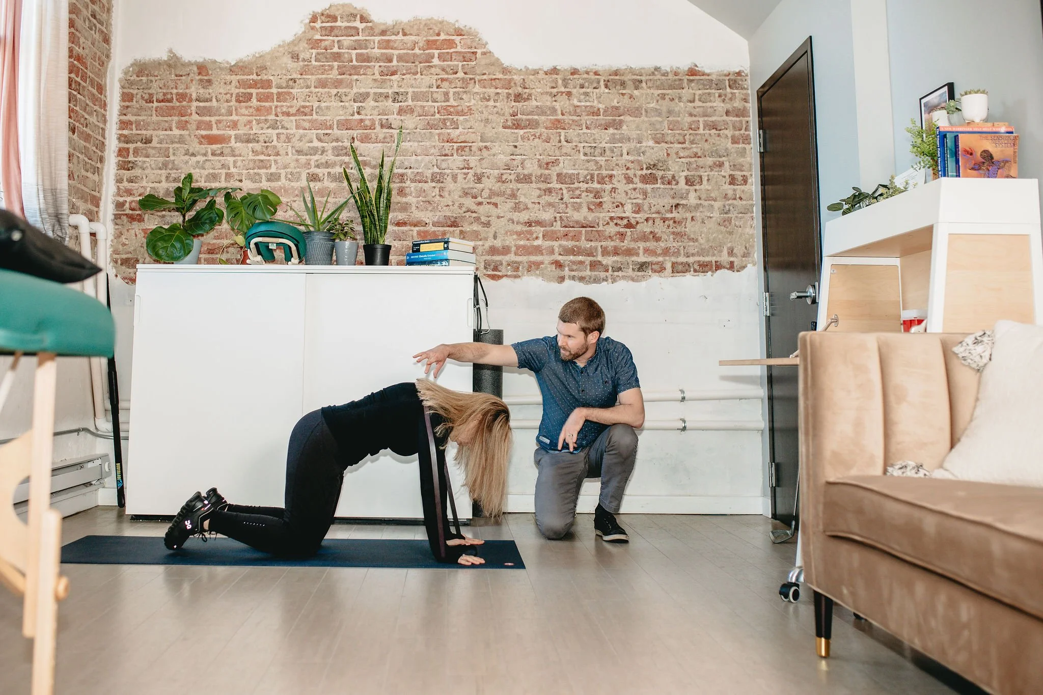 Man in blue shirt instructs blonde woman how to do a back excercise on a yoga mat
