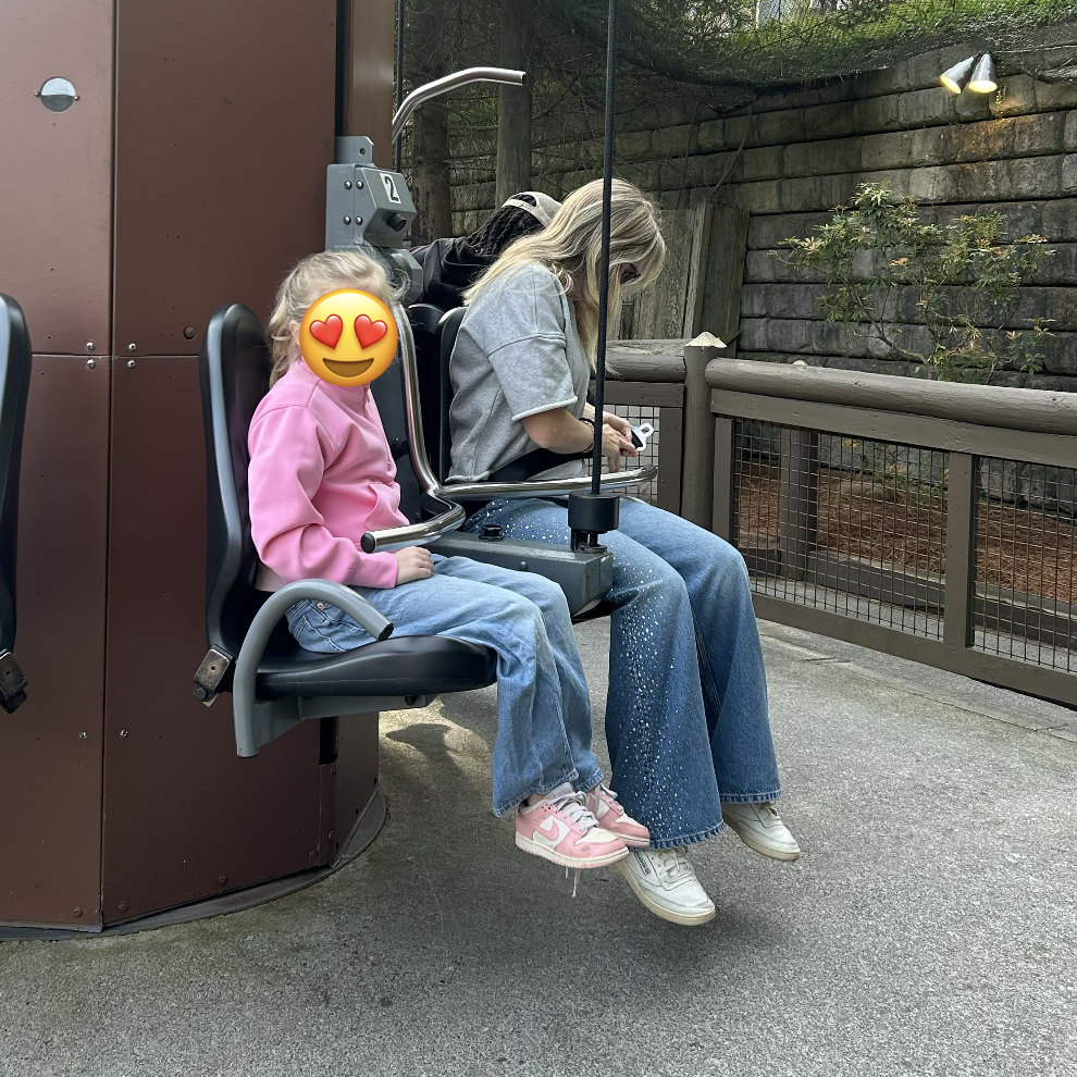 Maggie, the author, looks down to buckle herself into a theme park ride. Rhinestones are sort of visible on her jeans. Her daughter cheerfully looks on.