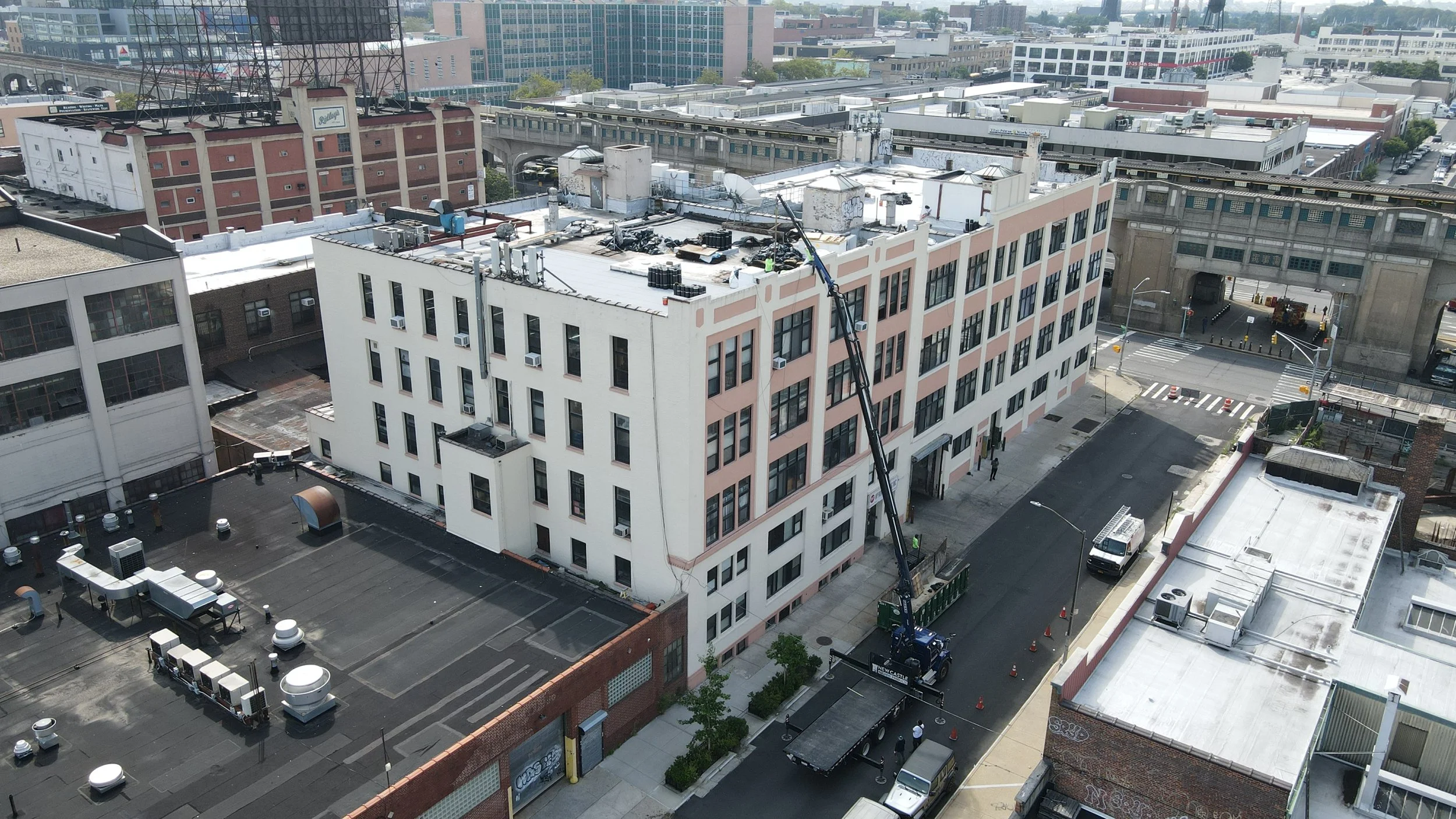 Construction crew operating a boom lift to repair or clean the roof of a multi-story building in an urban area.