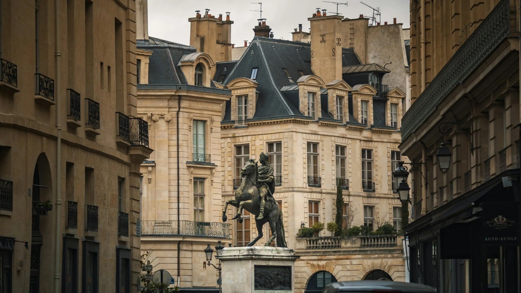 Une place urbaine avec un monument en bronze représentant un homme à cheval au centre, entourée de bâtiments en pierre de style parisien.
