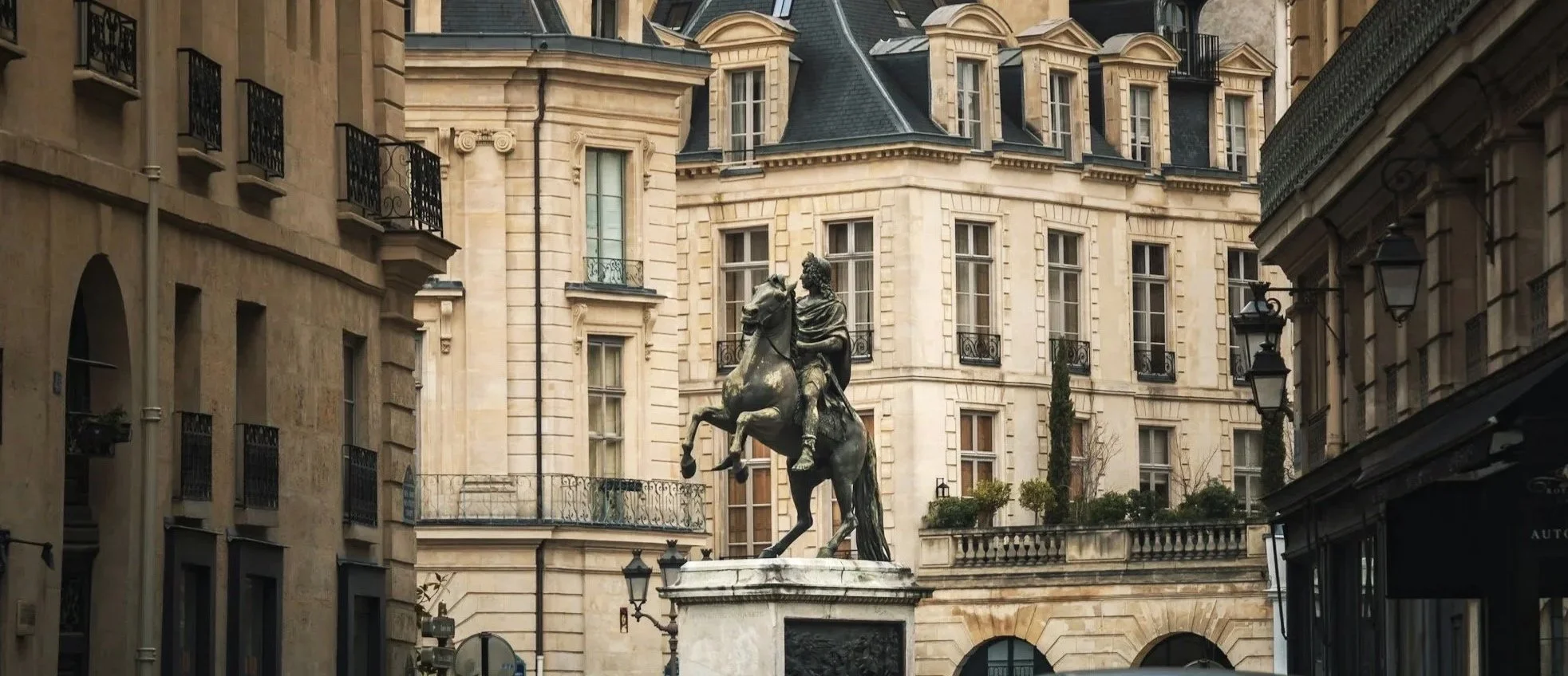 Une statue en bronze représentant un chevalier sur un cheval, située dans une cour urbaine avec des bâtiments en architecture classique parisienne autour.