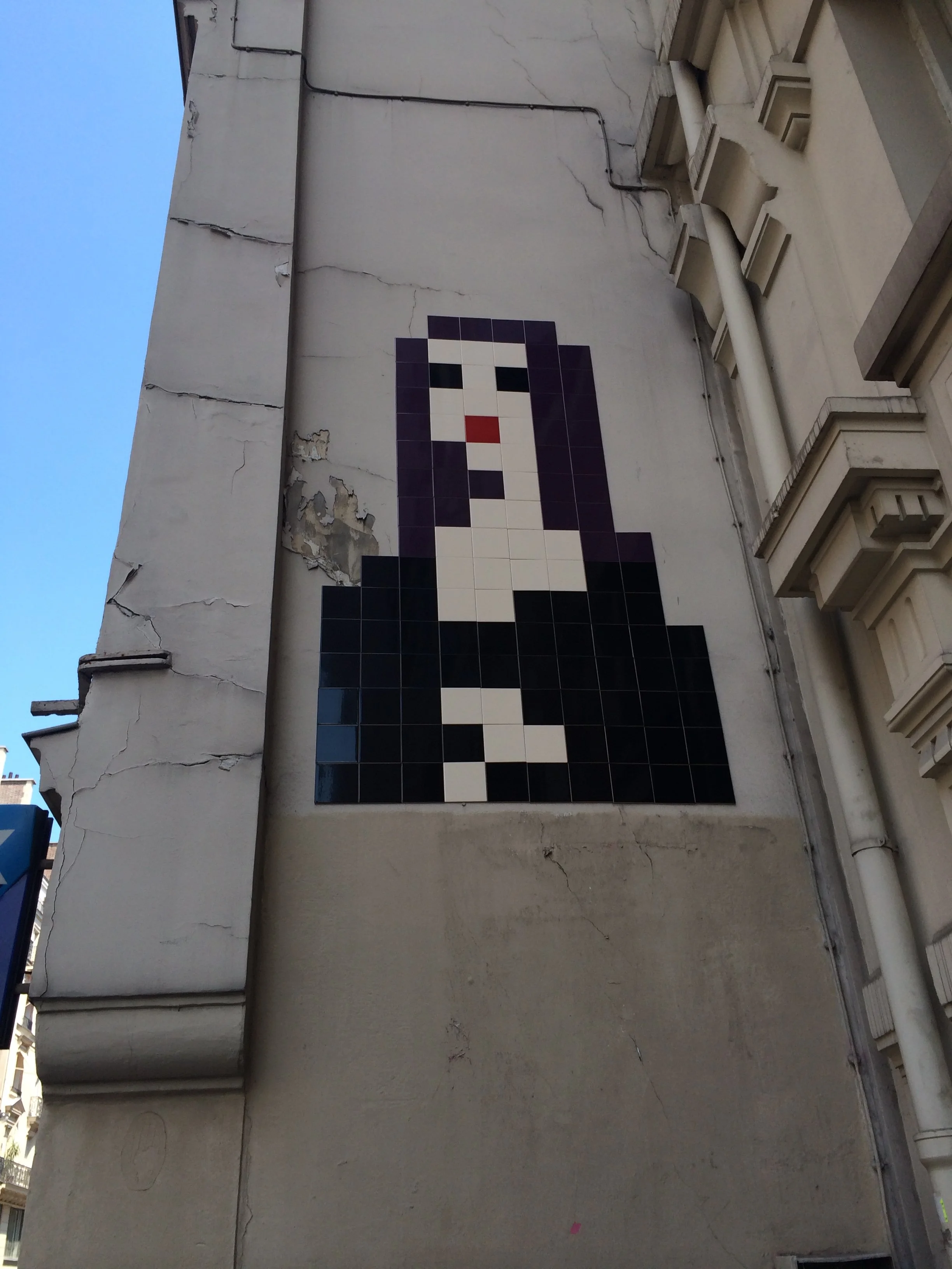 Mosaic of a woman with long dark hair, red lips, and a black shirt, painted on a weathered wall.