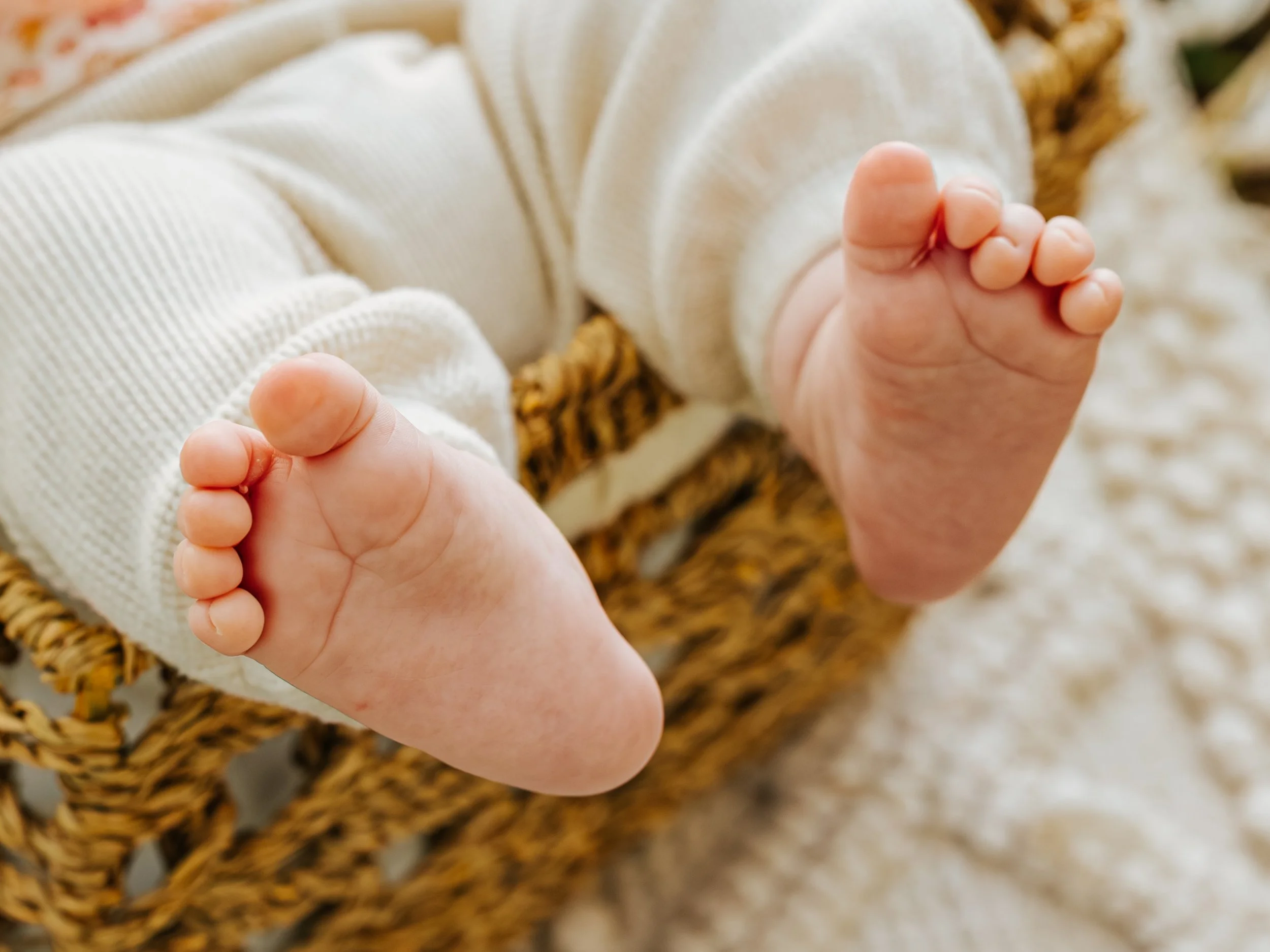 Close-up of a baby's hands holding a white blanket with a wicker basket and patterned fabric in the background.
