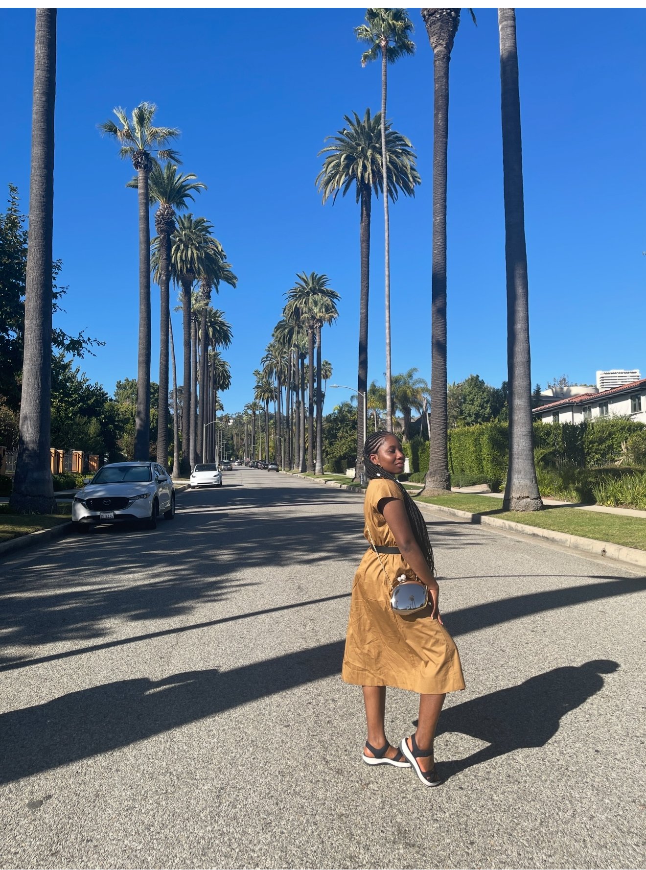Close-up of a man with curly dark hair, wearing clear glasses, a nose ring, and a dark green sweater, looking to the right against a plain background with a green plant visible on the right.