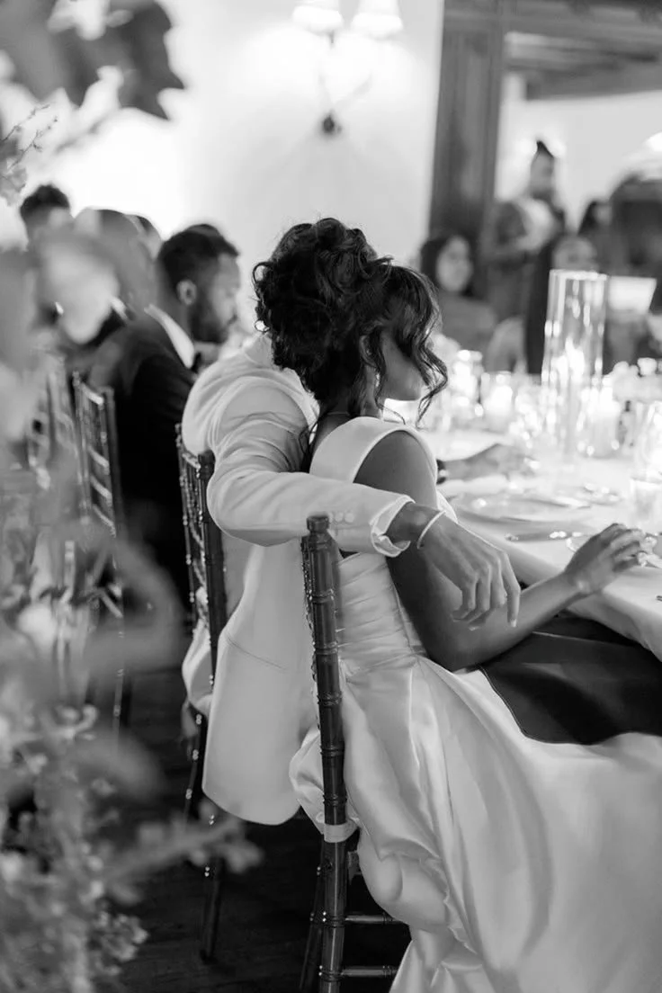 A woman smiling with short black hair, wearing a blue top, standing among green plants.