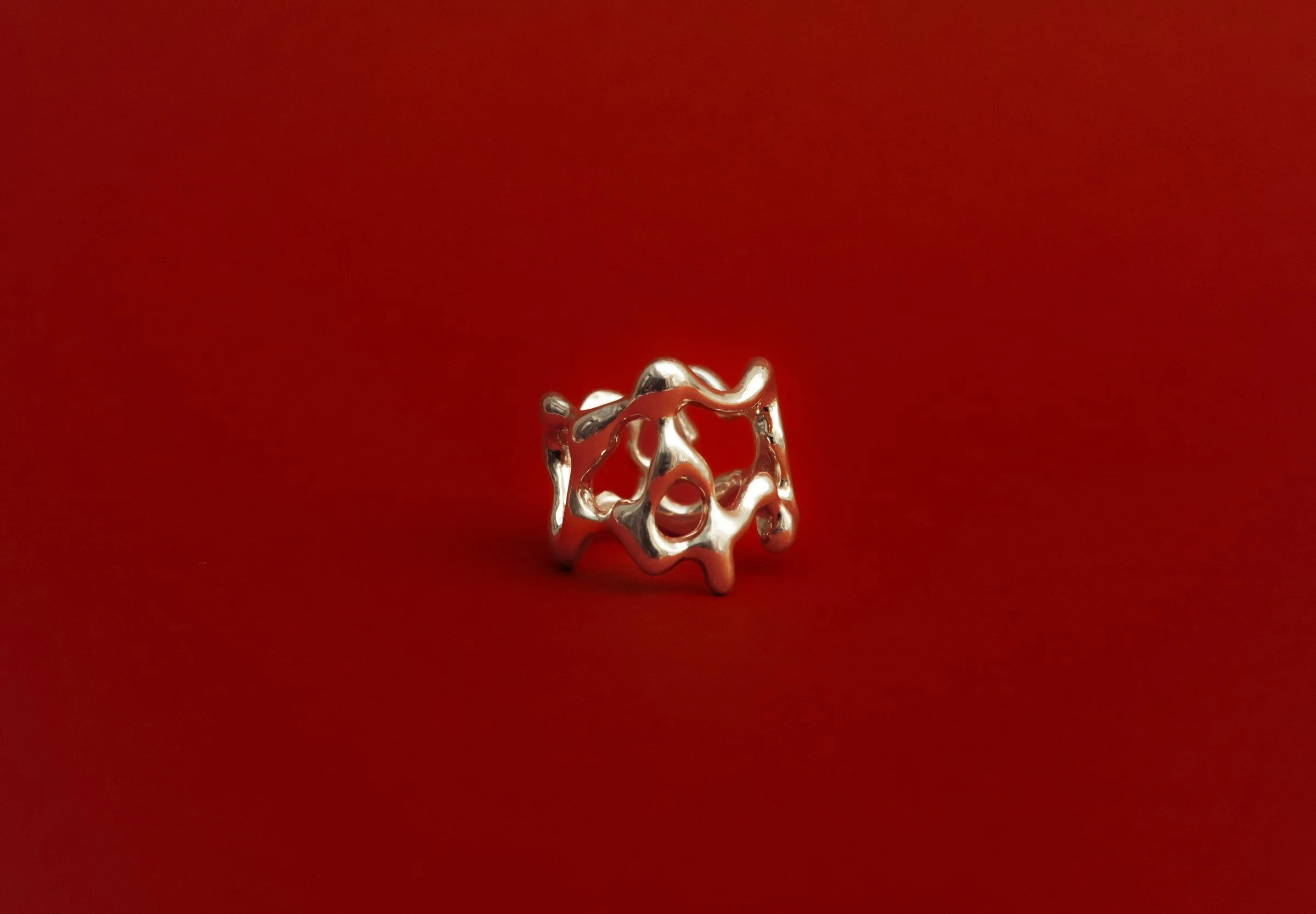 A hand-crafted, 925 silver abstract, organic shaped, sculptural ring on a red background.