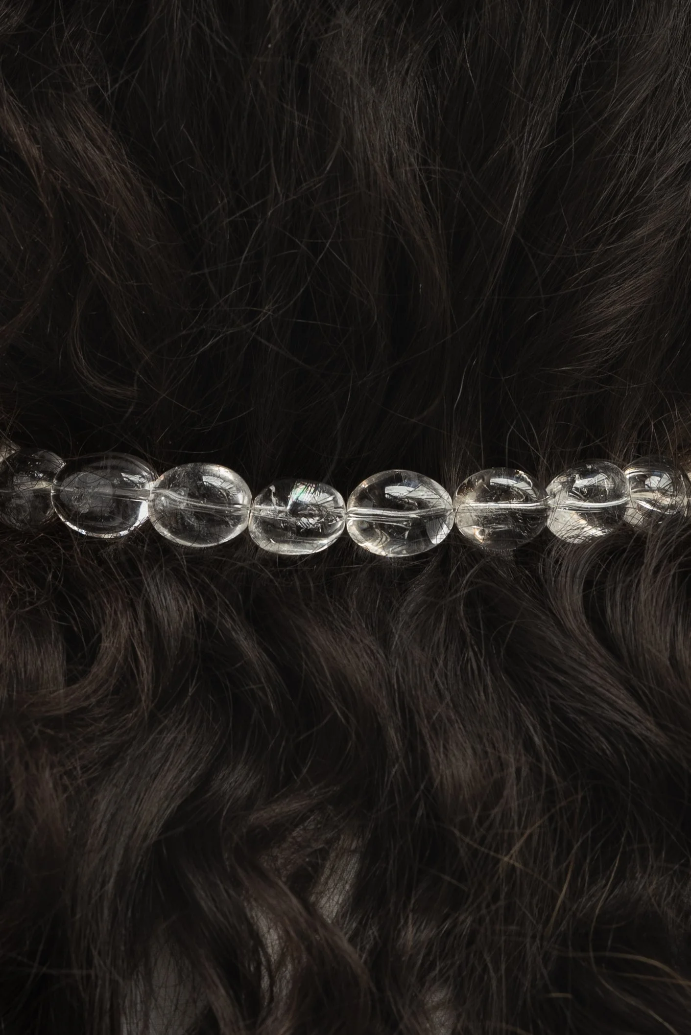 Close-up of dark curly hair with an elegant necklace made of round, clear quarz beads.