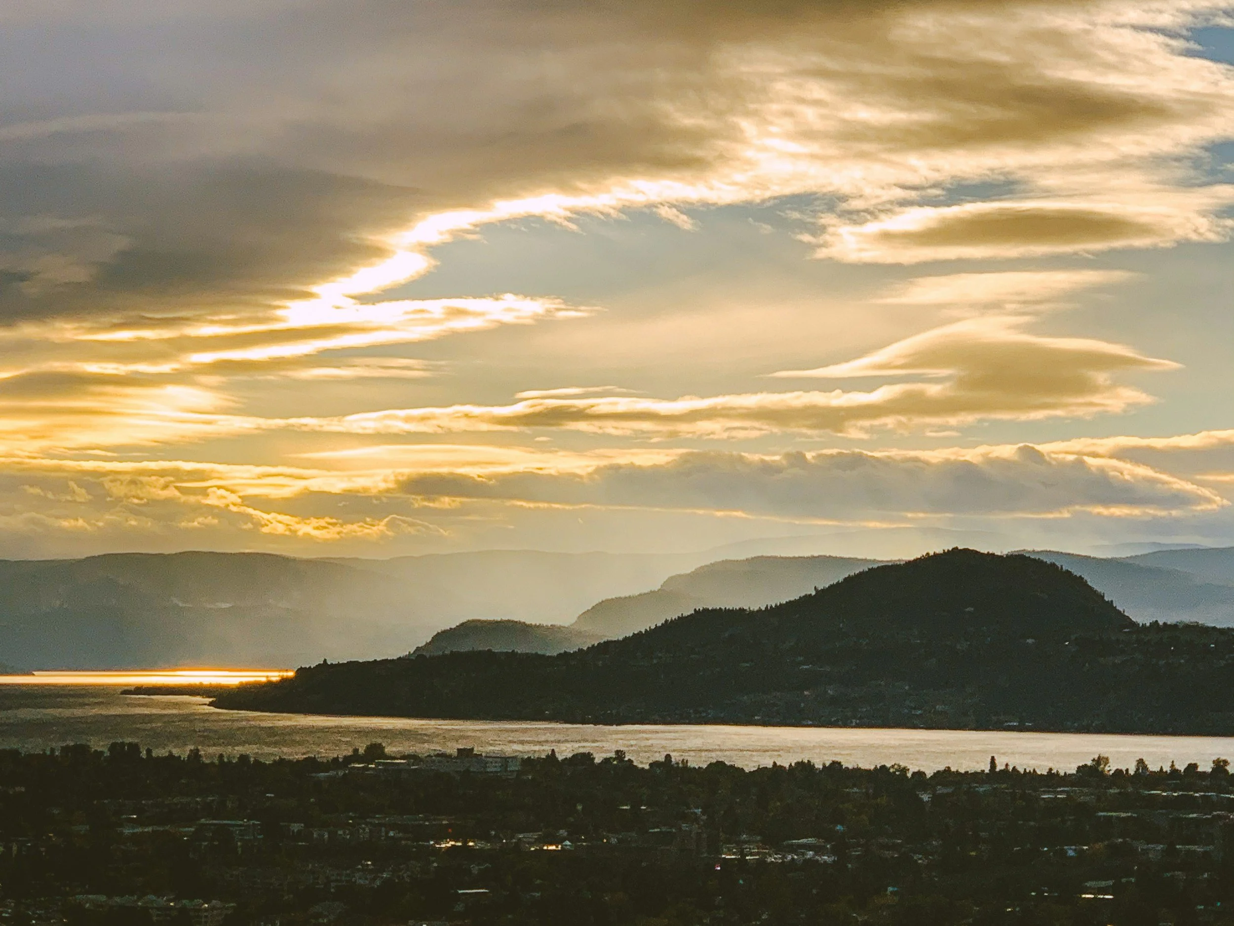 Sunset over a valley with mountains and a body of water, with clouds in the sky