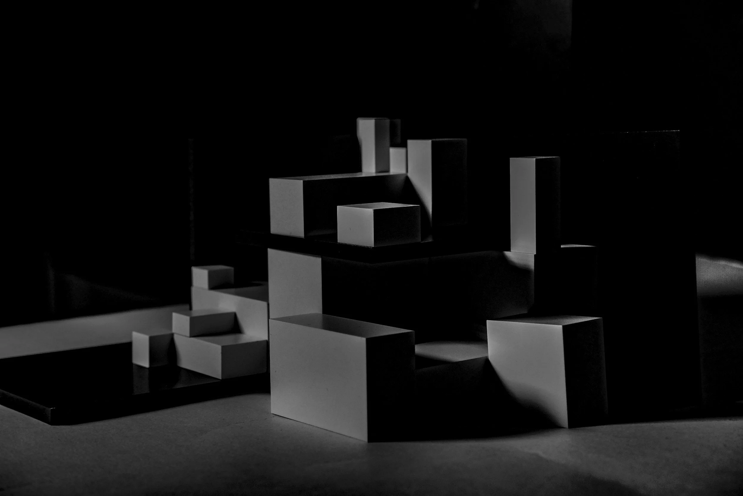 Black and white photo of various geometric paper or cardboard blocks arranged in a pattern with light and shadow effects, creating an abstract composition.