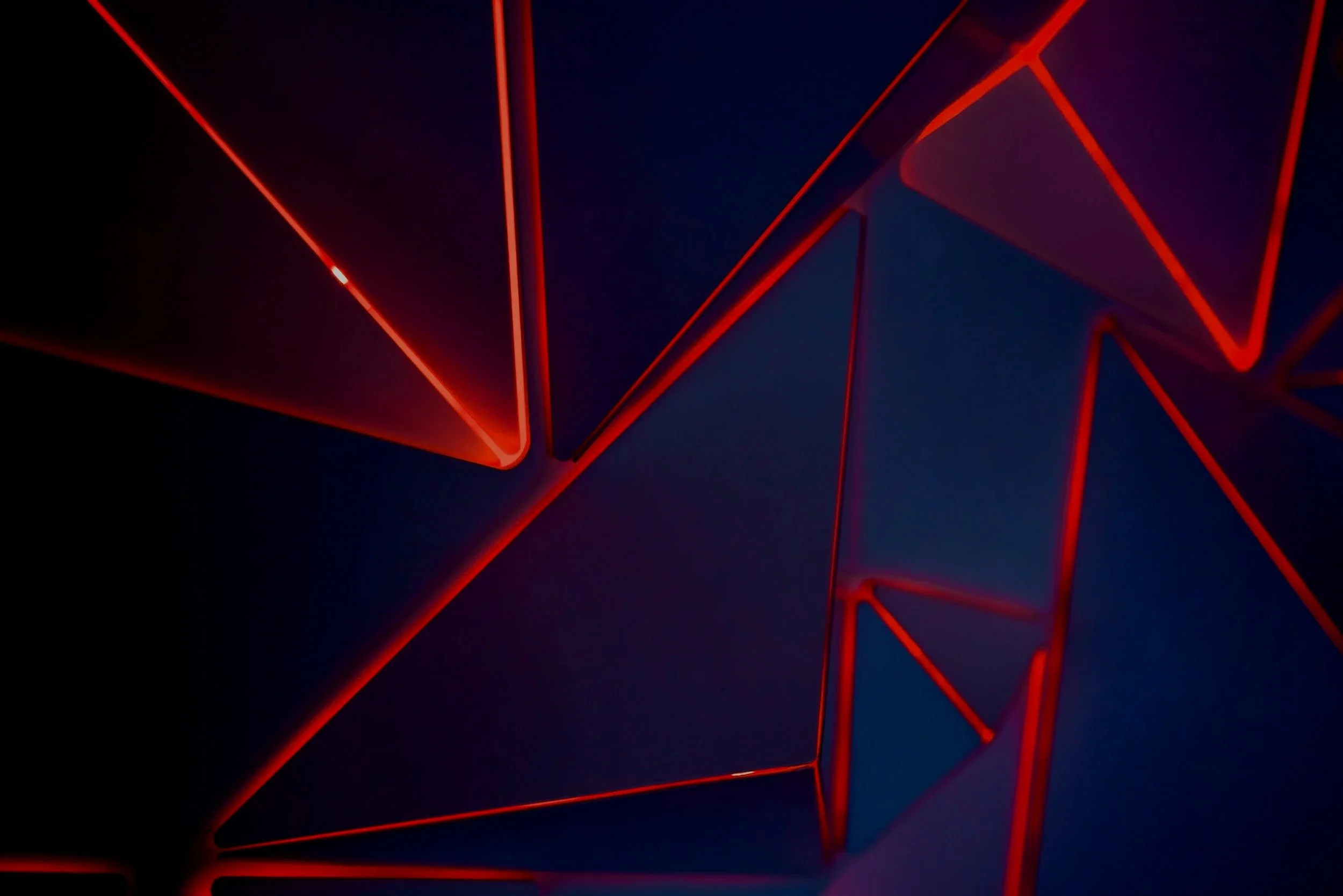 Close-up of an abstract geometric neon light art installation with red glowing lines against a dark background.