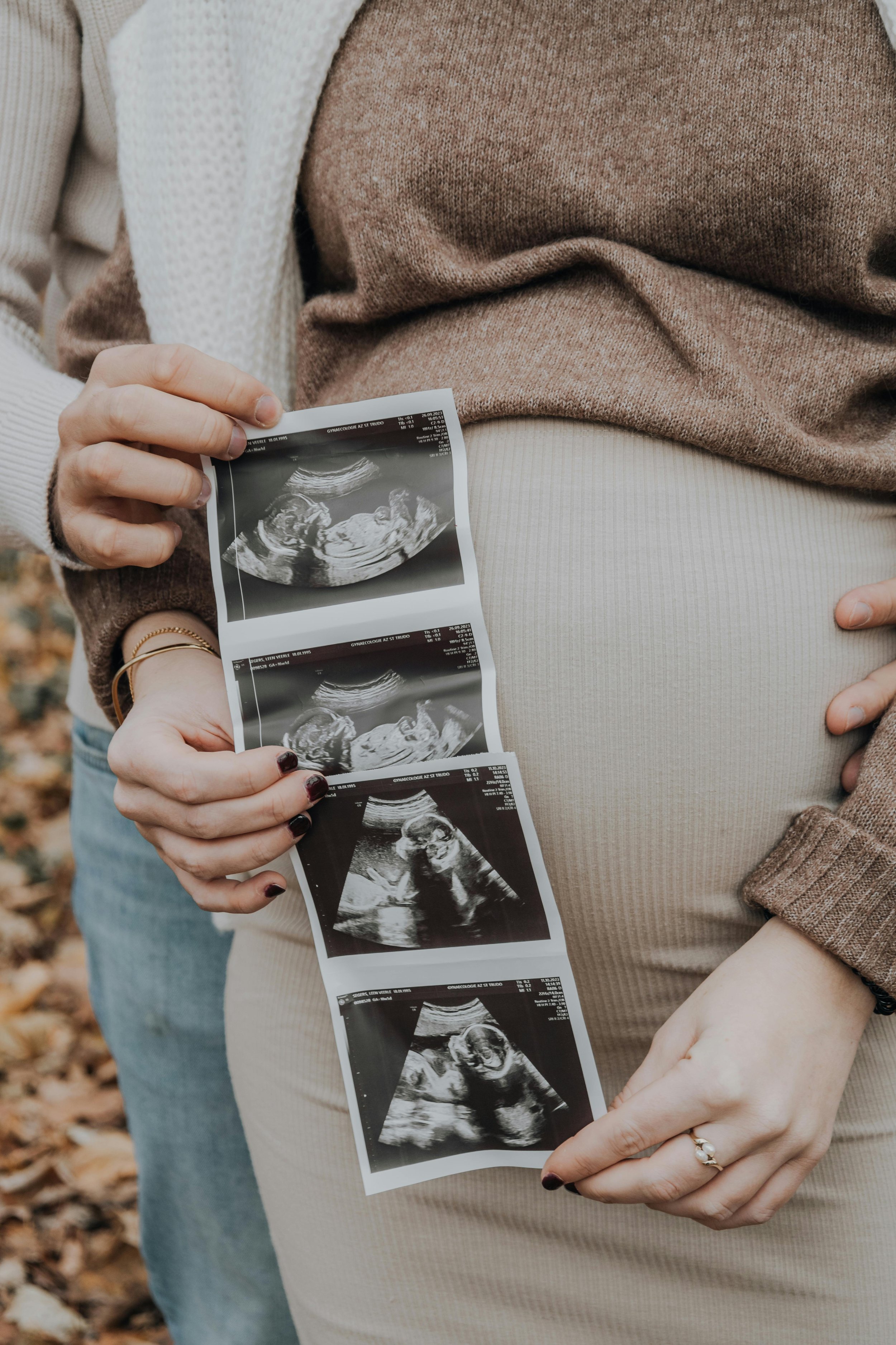 Person holding ultrasound images of a fetus with autumn leaves on the ground in the background.