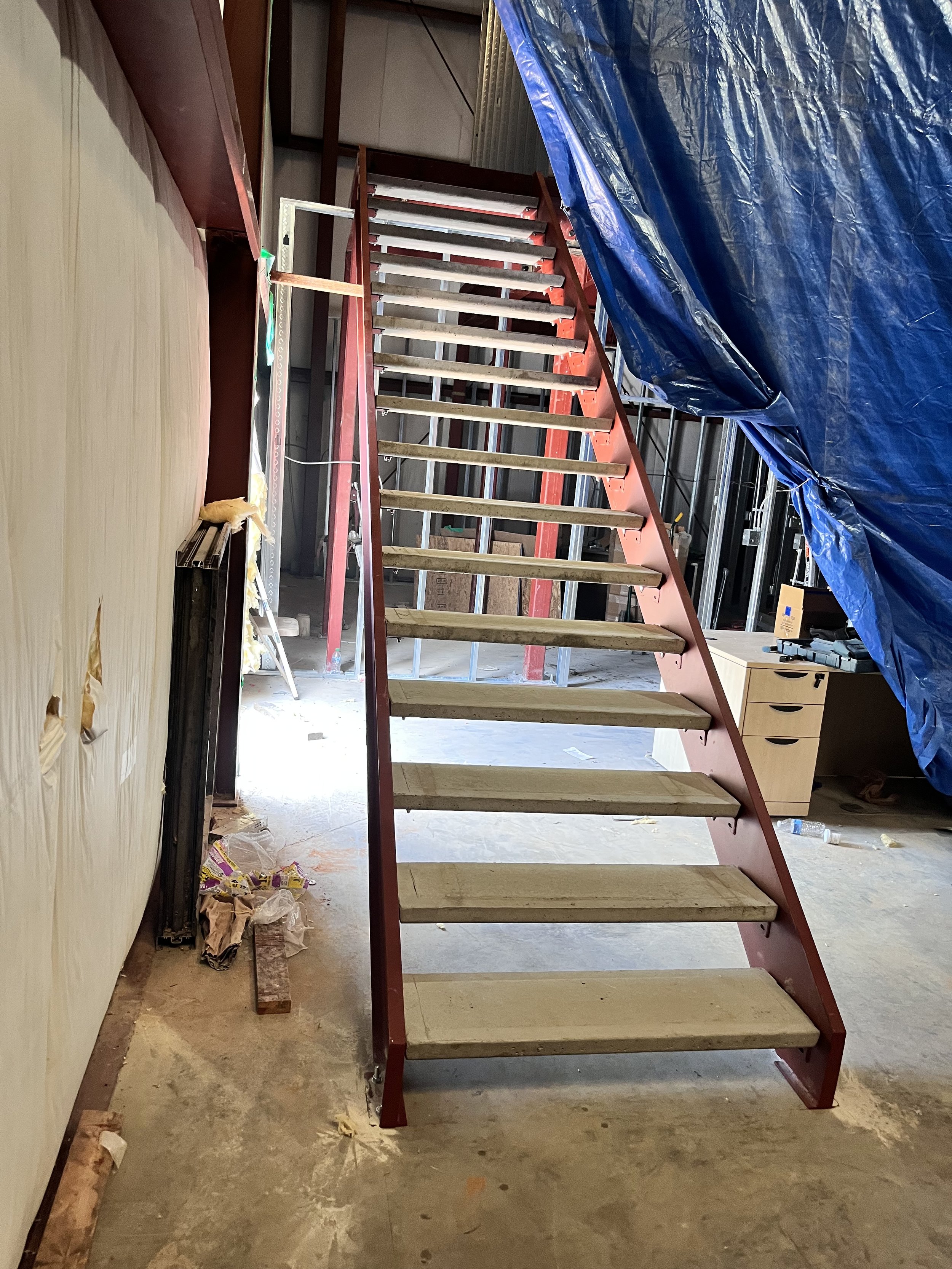 Indoor construction site with metal-framed stairs, blue tarp, and scattered construction materials.