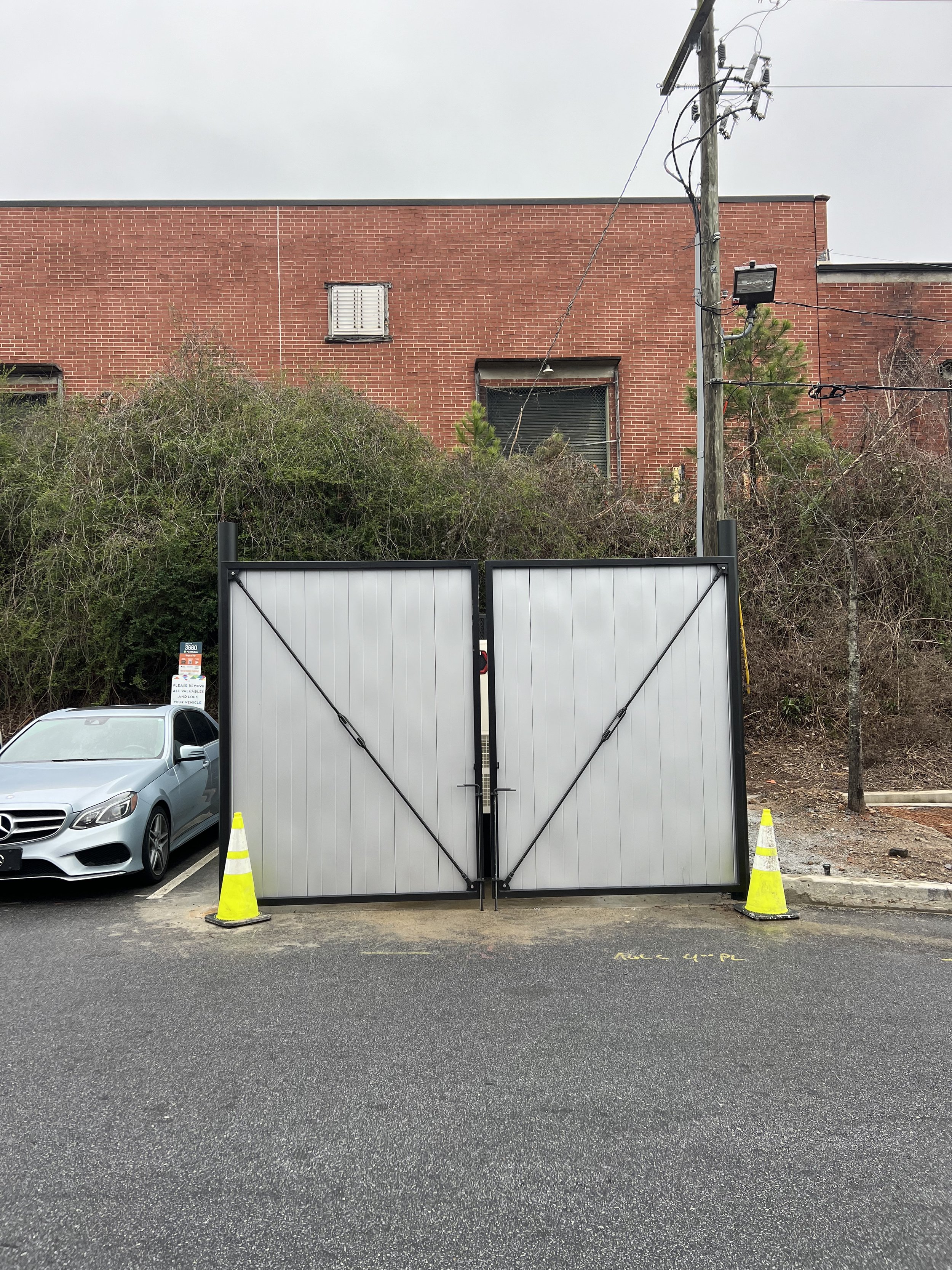 Metal gate with traffic cones, brick building, and parked car